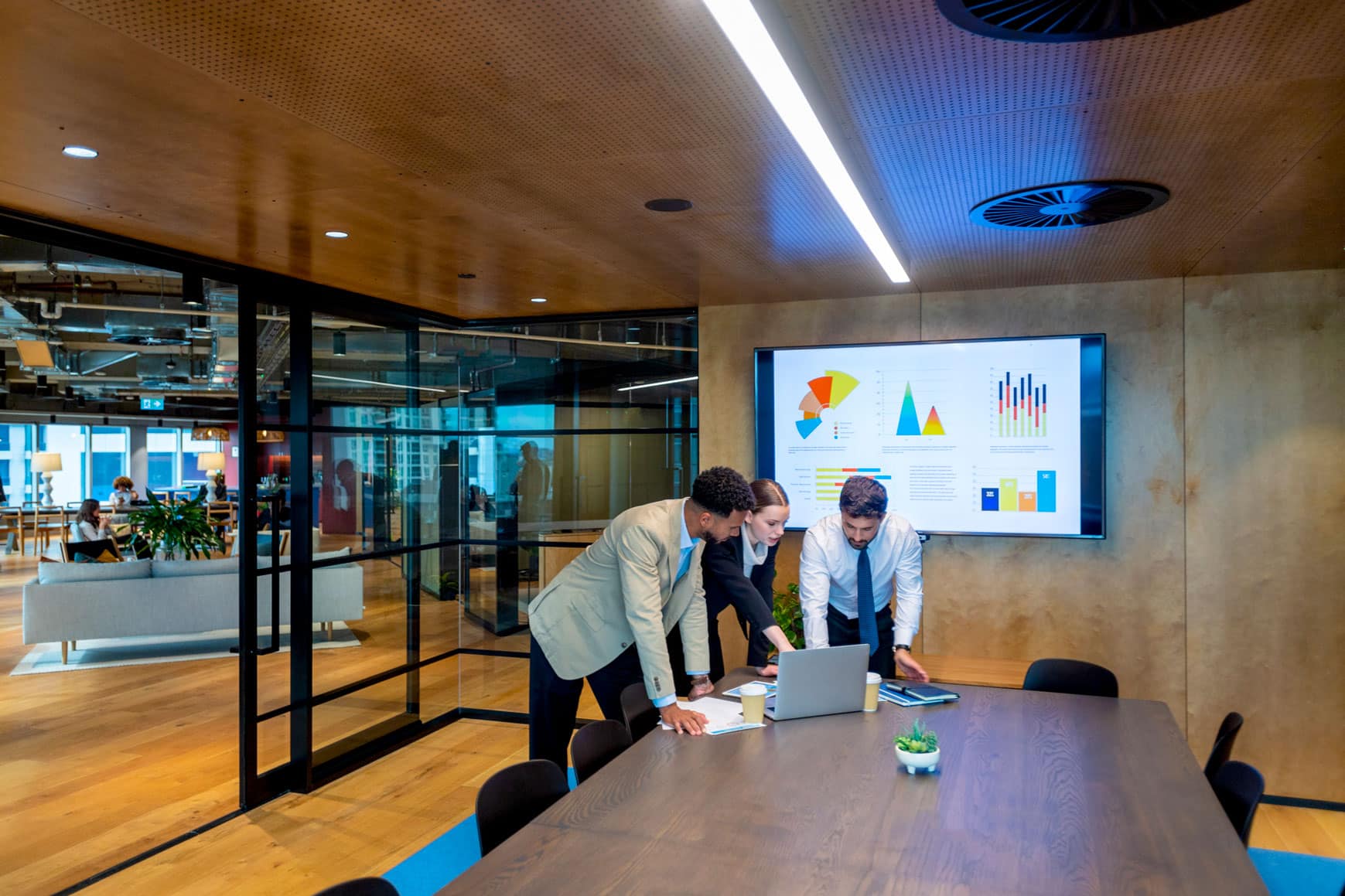 Three people reviewing charts on a laptop while discussing change management consulting services.