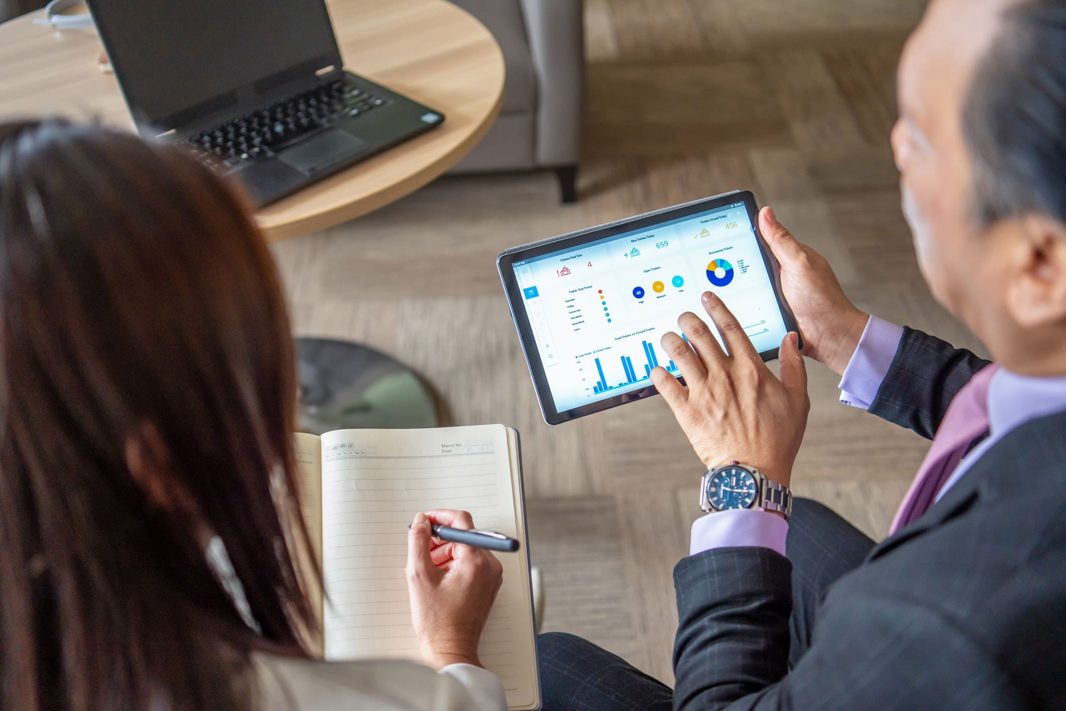 Two people from Expense Reduction Advisory review charts on a tablet as one takes notes.