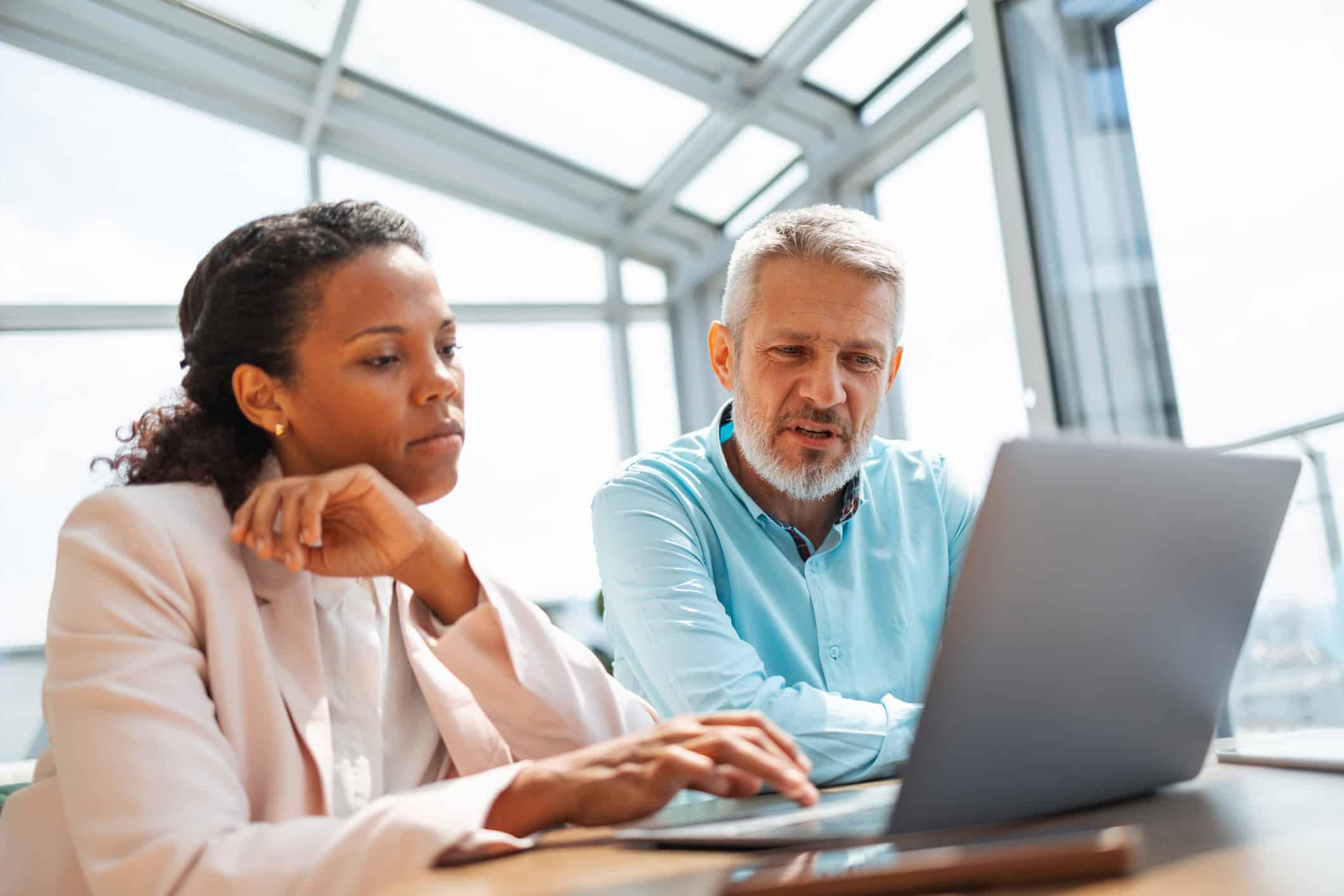 Two Corporate Tax Consultants reviewing data on a laptop in a bright, modern office setting.