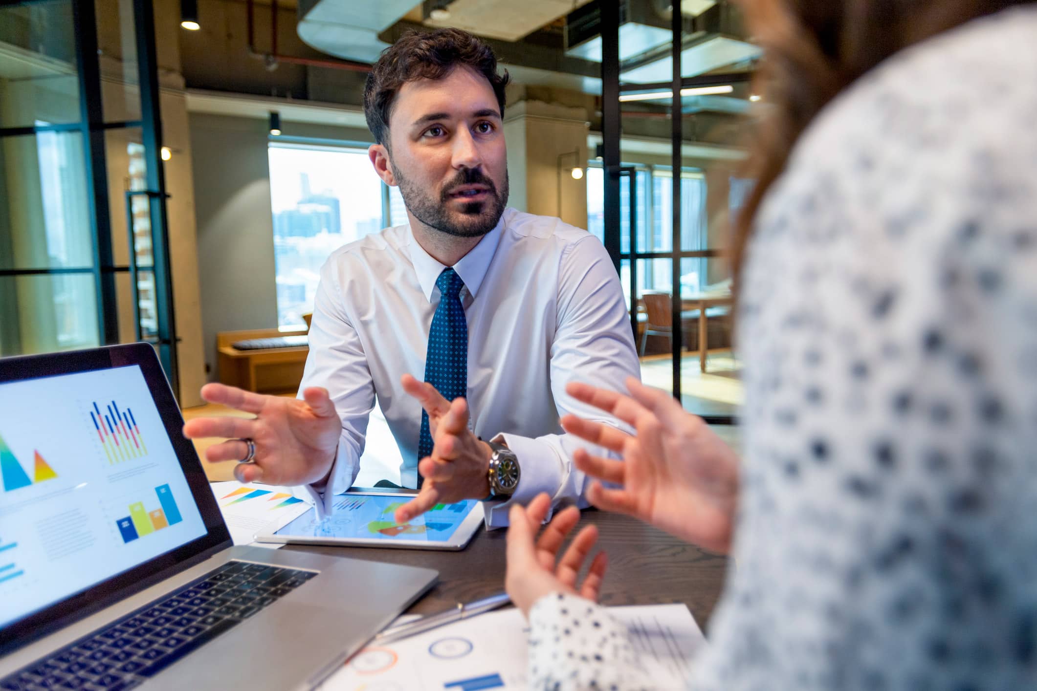 Man in business attire discussing Practice Mix Optimization with a colleague in a modern office.