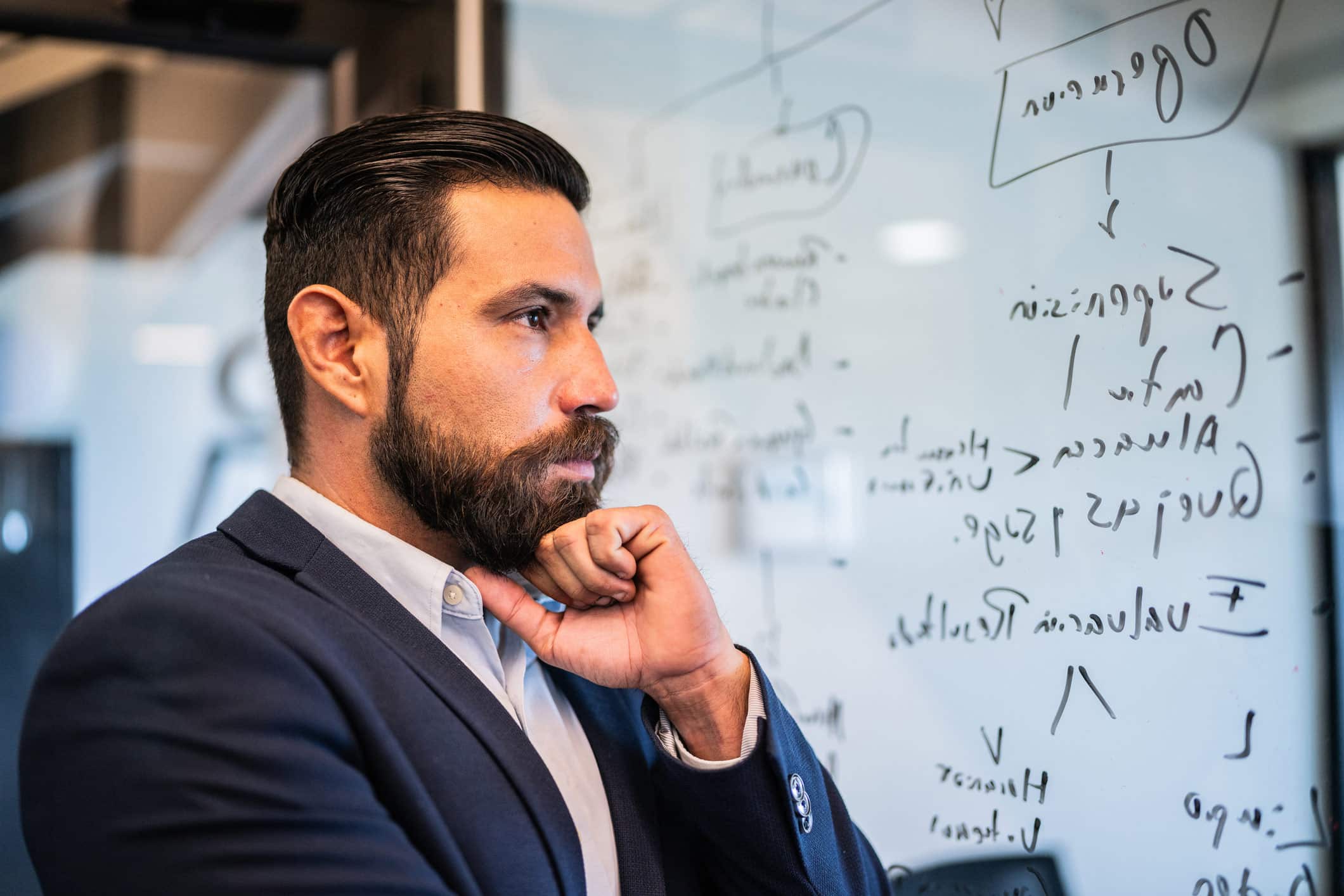 Man in suit thinking before a glass wall, as Witness Preparation Consultants assist with strategy.