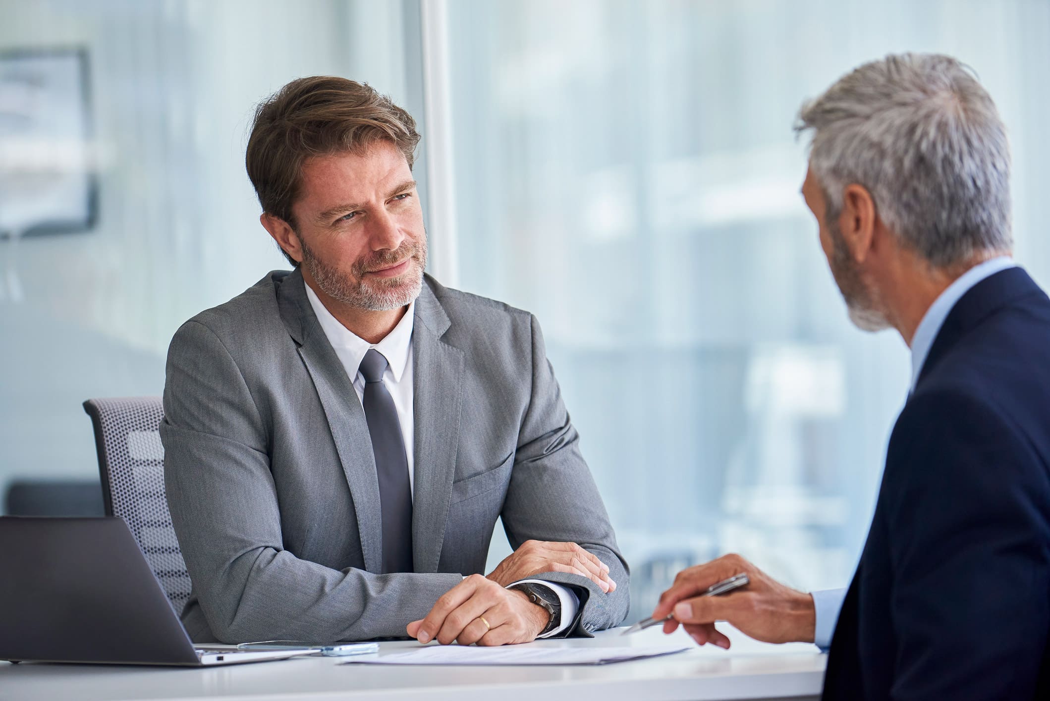 Two businessmen in suits discuss strategy at a Corporate Tax Consulting Firm office.