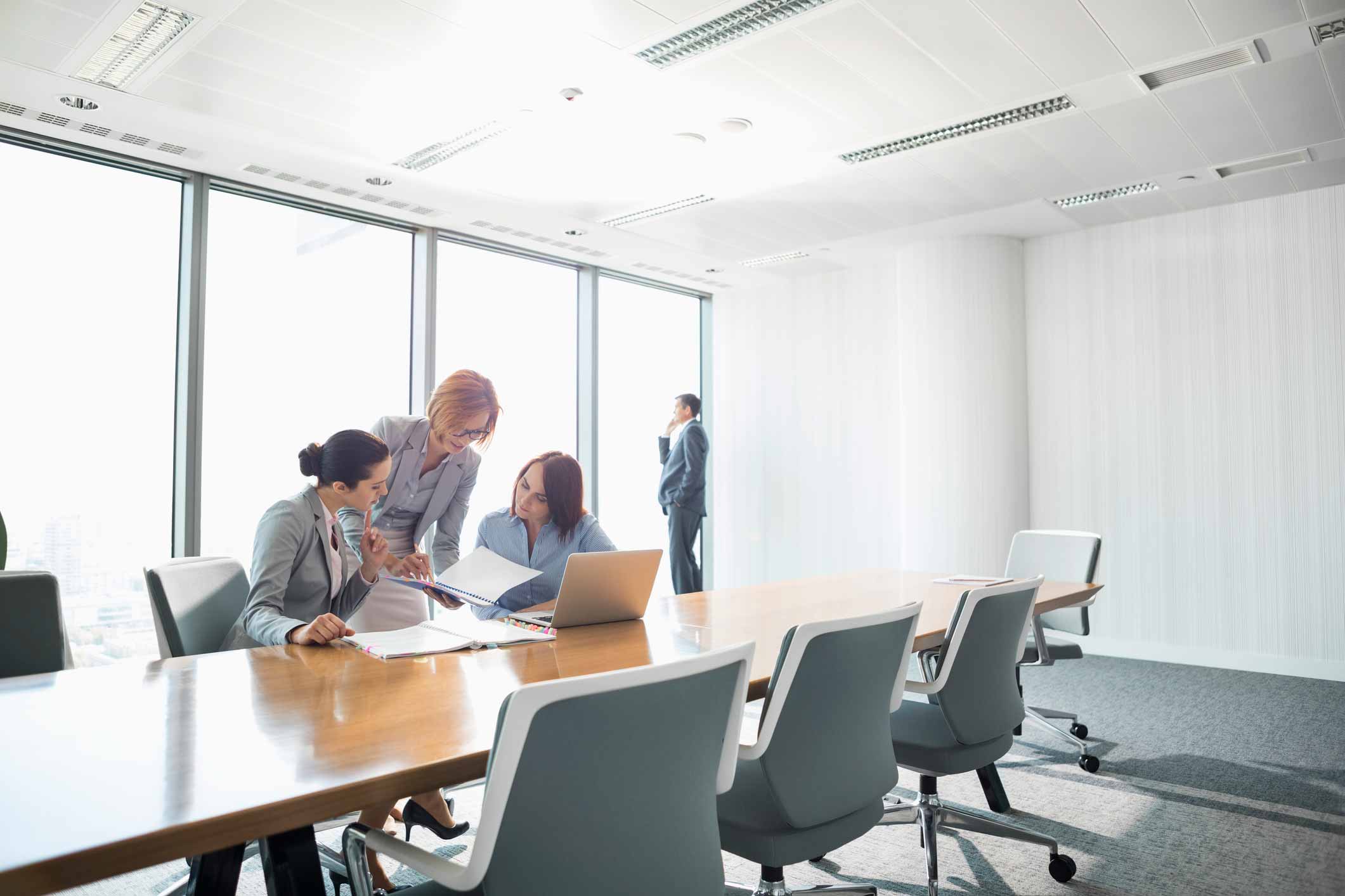 Three women review documents at cyber incident response consulting firm; a man stands by the window.