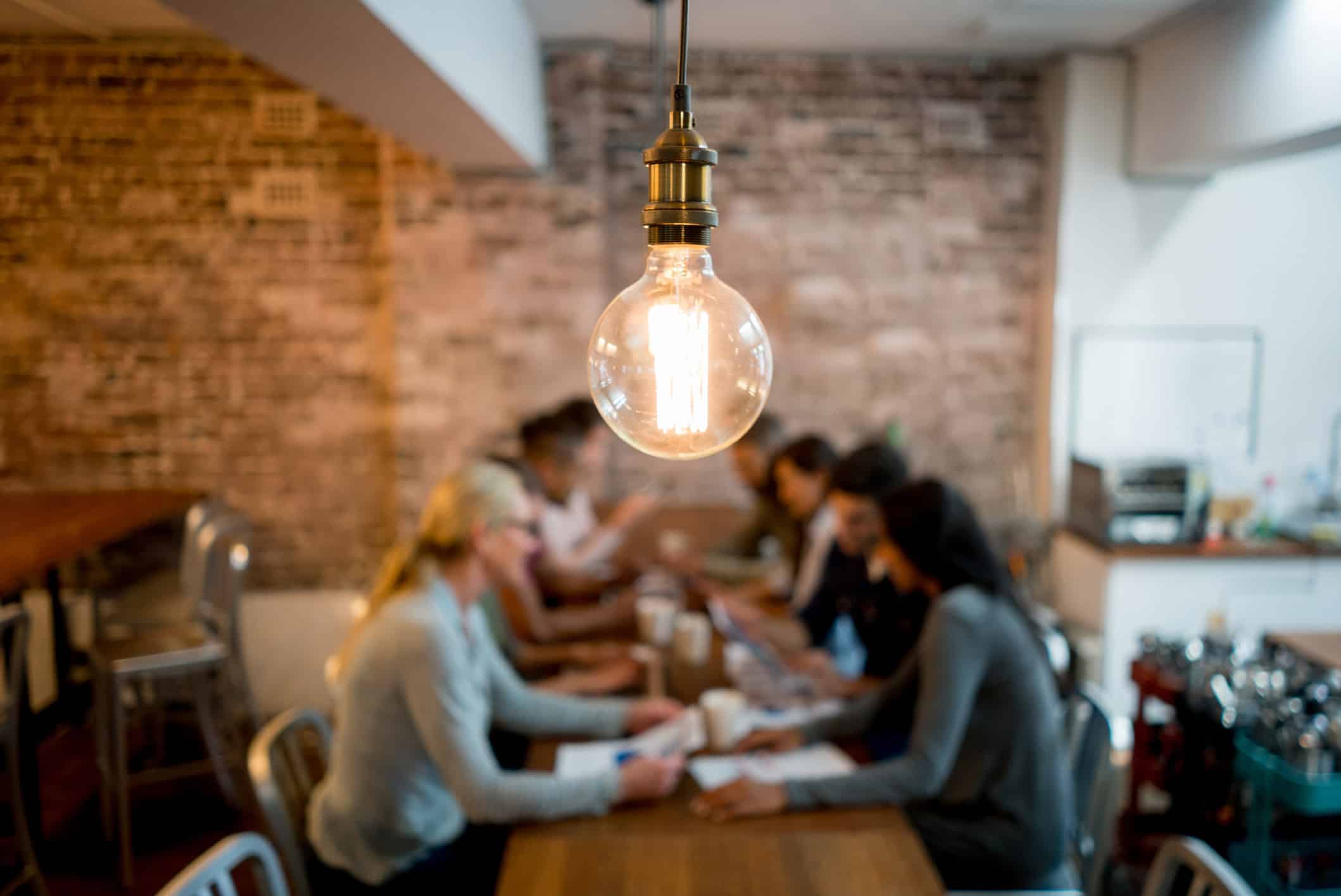 A lit lightbulb in focus, with a law firm marketing strategy team collaborating in the background.