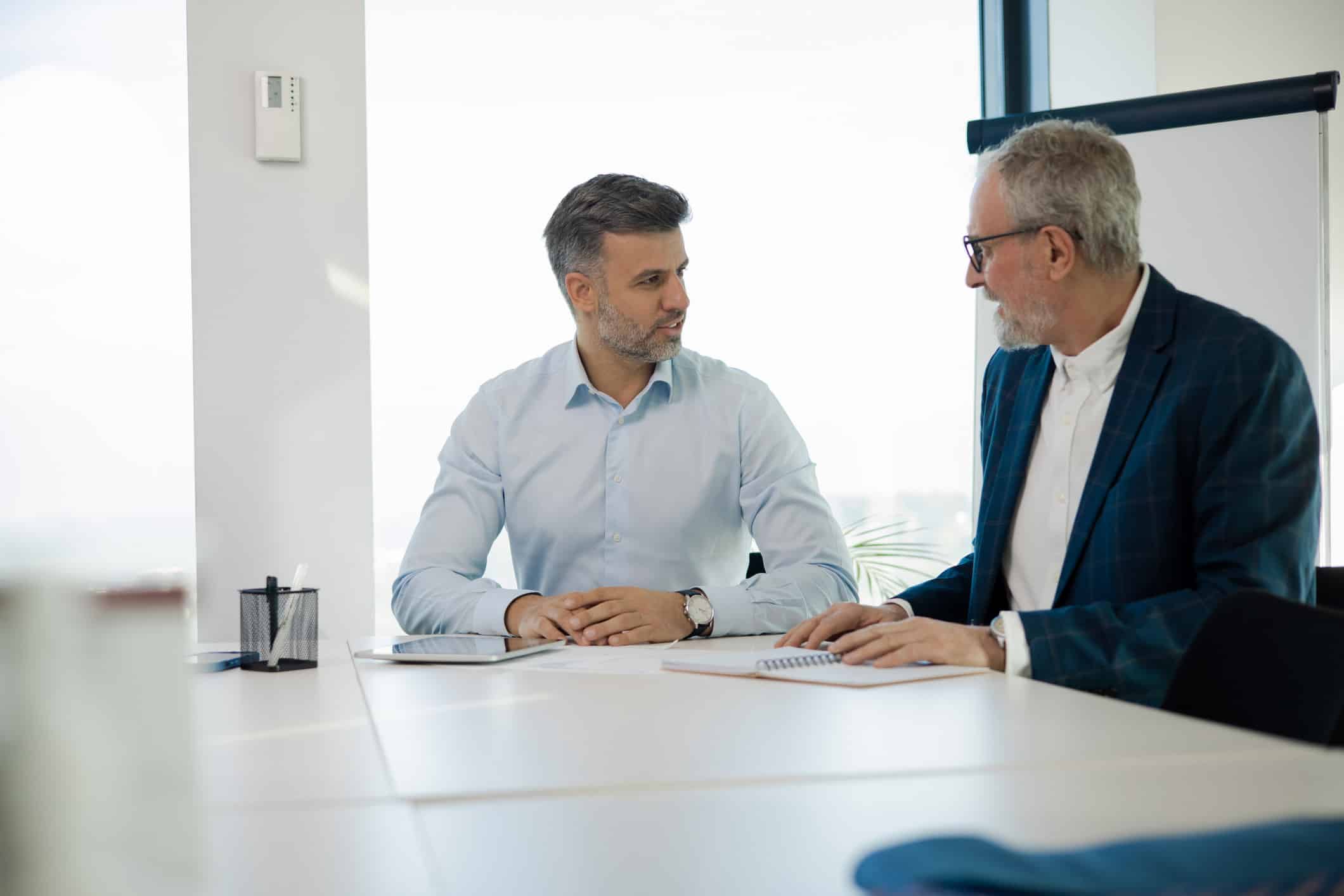 Two men in business attire discuss Law Firm Marketing Advisory at a conference table in an office.