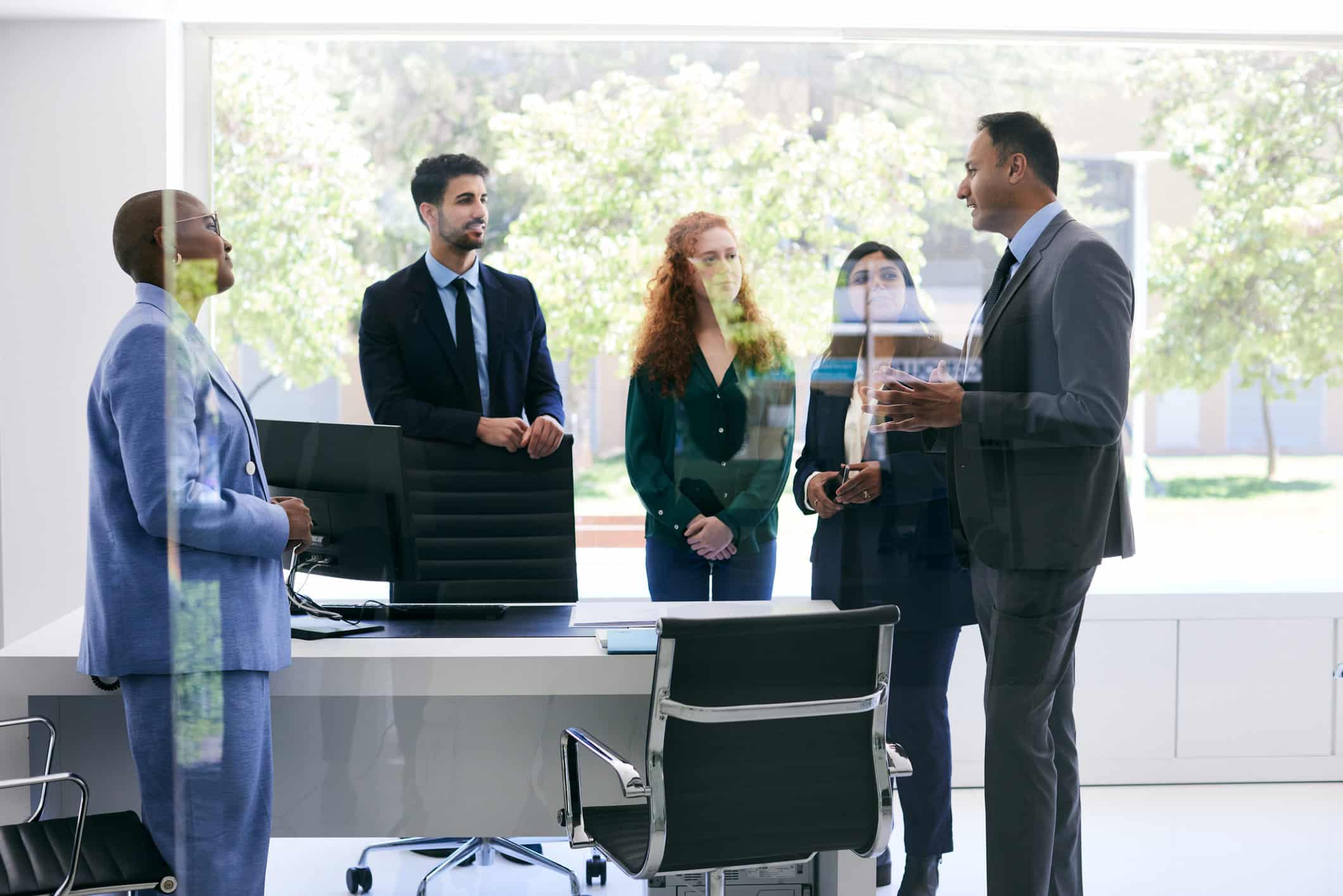 Five people in business attire meet with law firm succession planning consultants in a modern office.