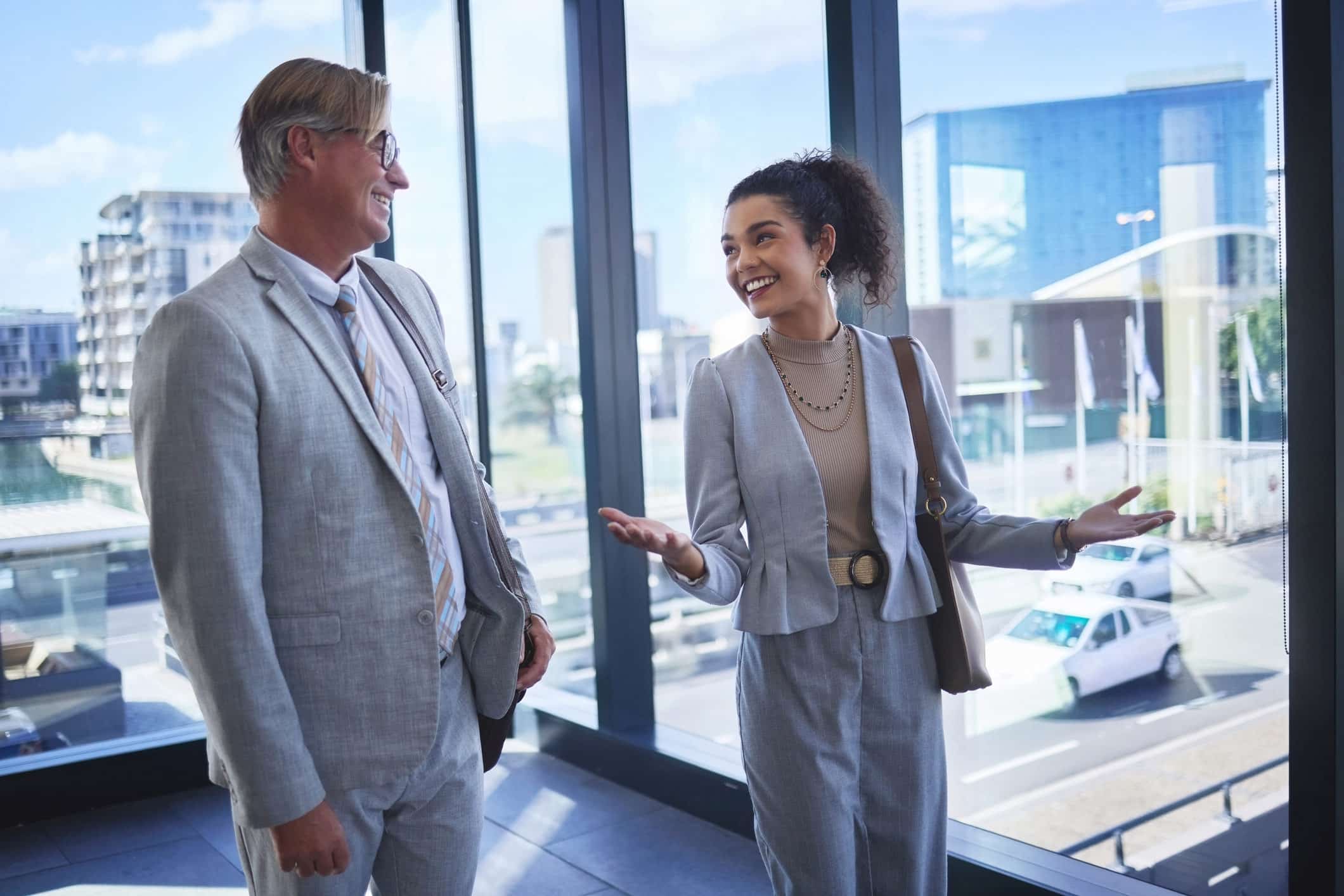 Two businesspeople discuss change management alignment by large windows in a modern office.