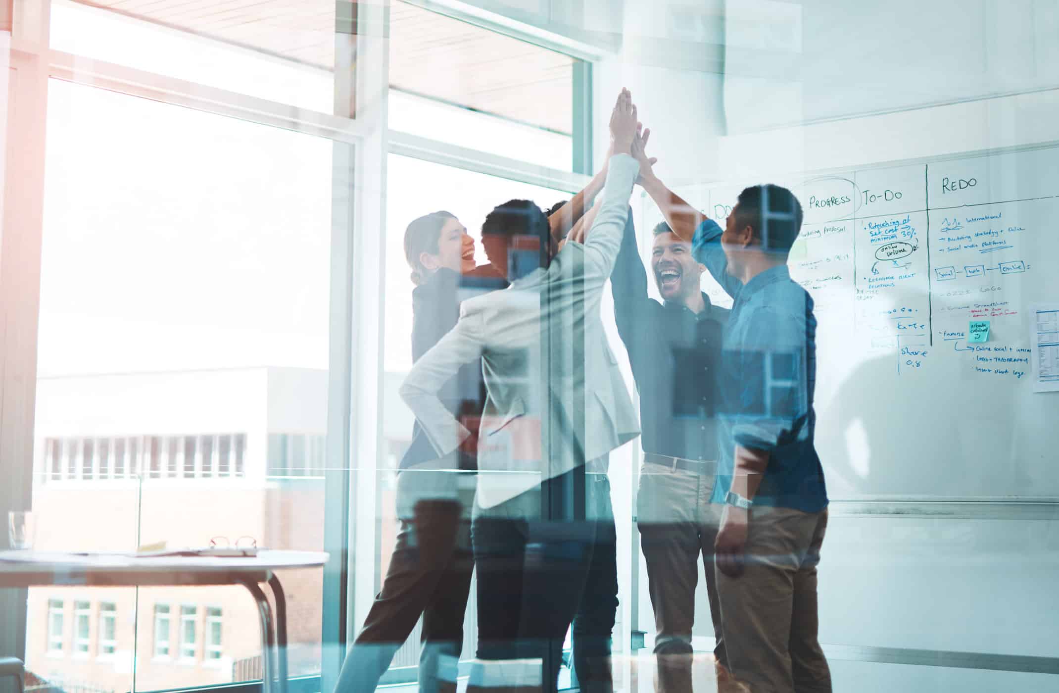 Five people in an office celebrate Leadership & Operational Governance with a group high-five.