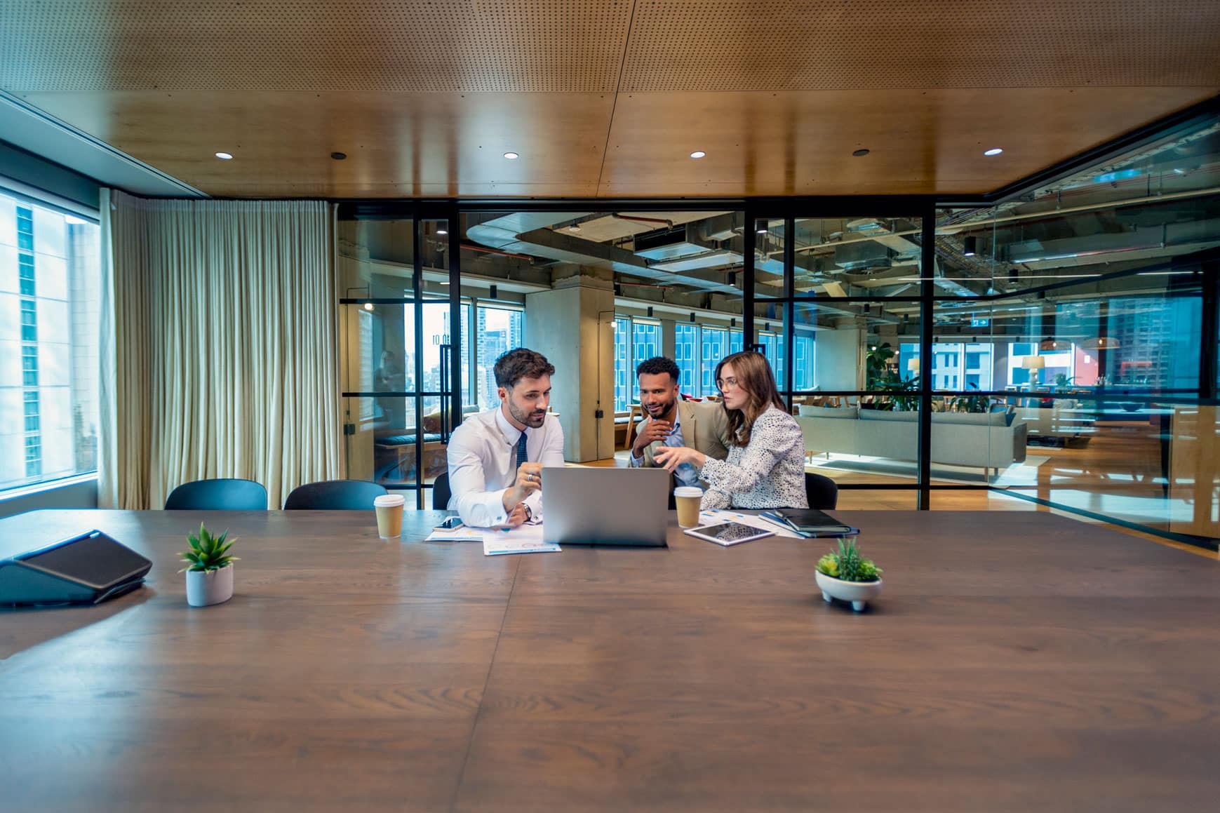 Three people at a Business Intelligence Consulting Firm look at a laptop in a modern office.