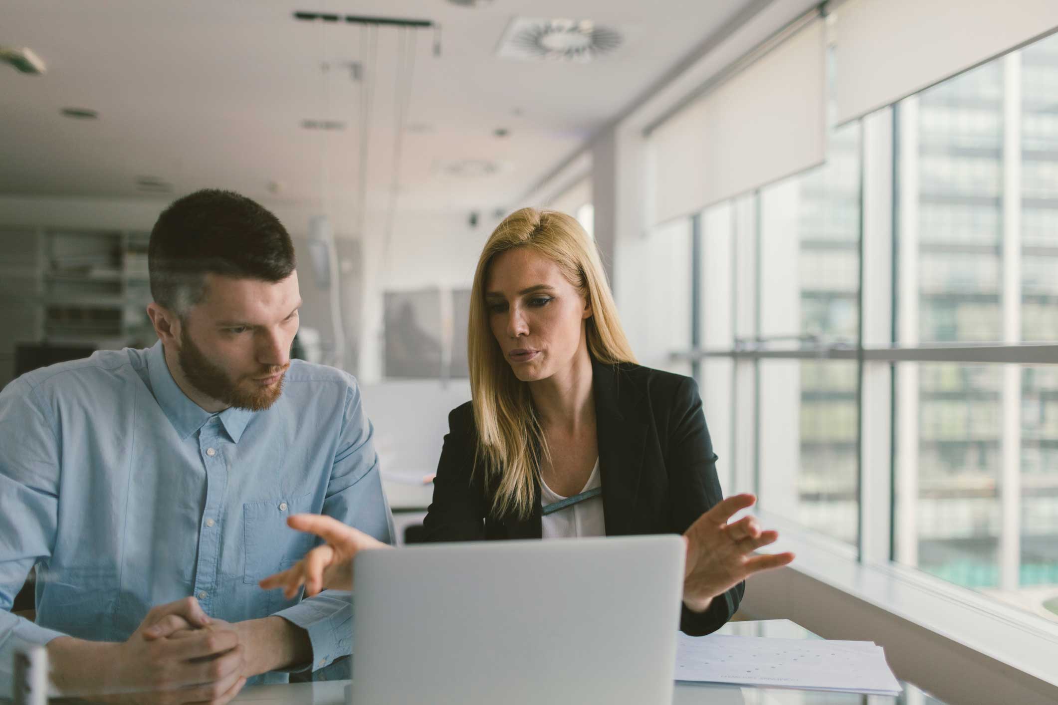 Two colleagues at a digital forensics consulting firm discuss work while viewing a laptop.
