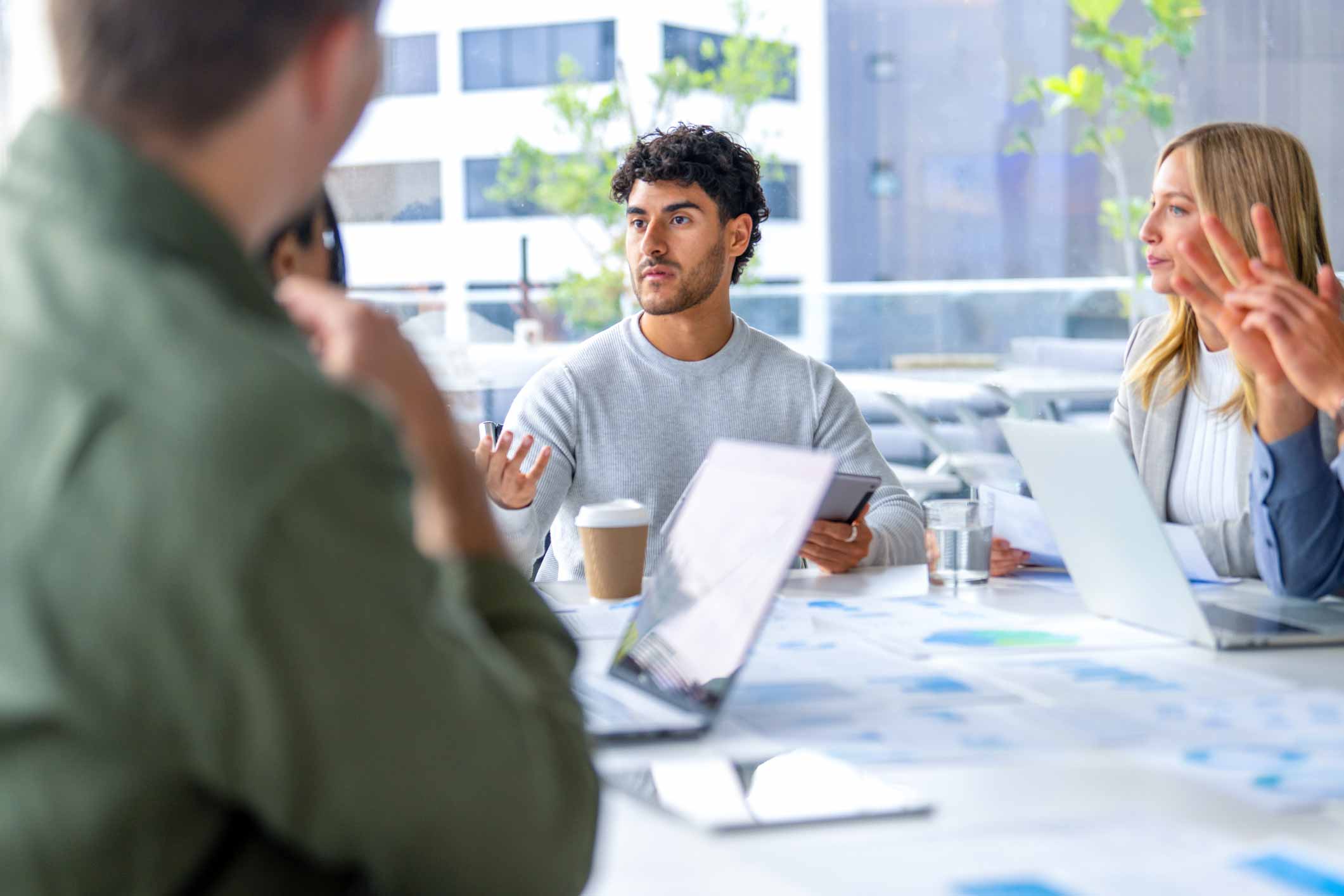Four Document Management Consultants discuss around a table with laptops in a modern office.