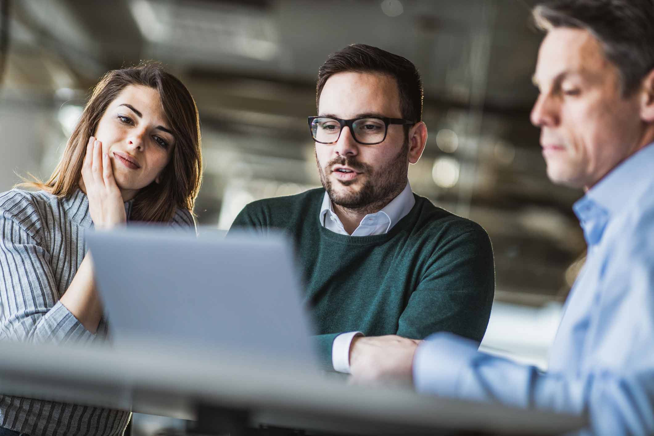 Three people discussing Law Firm Expense Management Consulting Services around a laptop in a office.