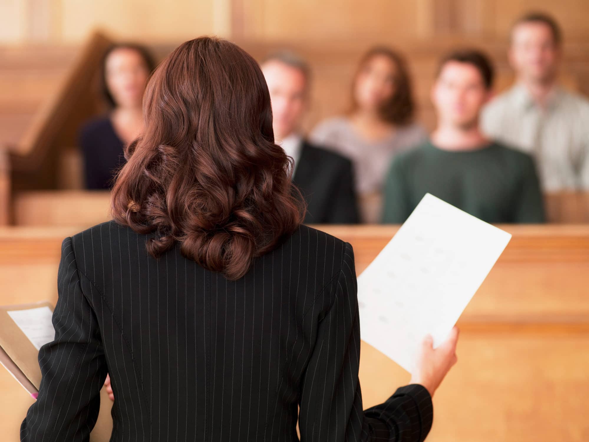 A woman in a suit presents business valuation documents to a jury in a courtroom.
