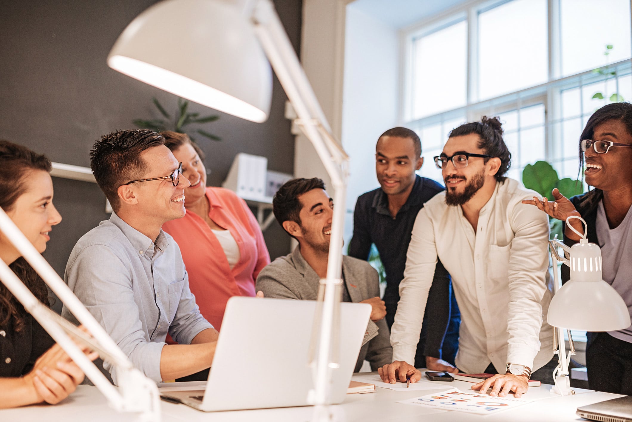 Six people discuss Law Firm Marketing Technology around a desk in a brightly lit office.