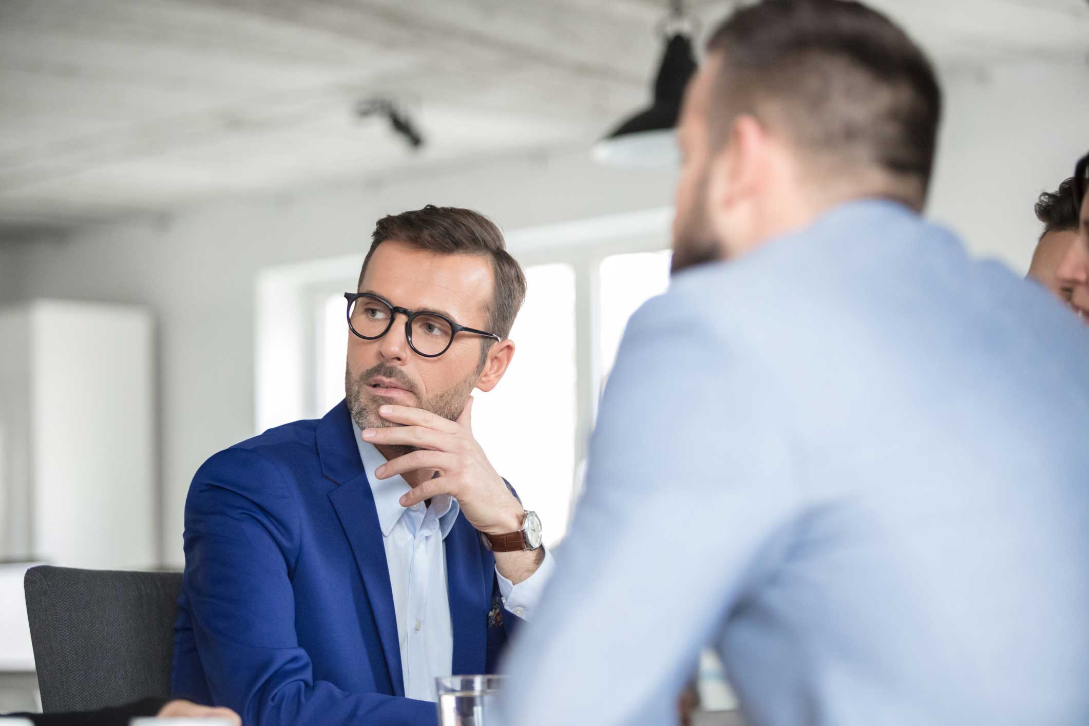 Man in blue suit and glasses listens thoughtfully during an information security consulting meeting.