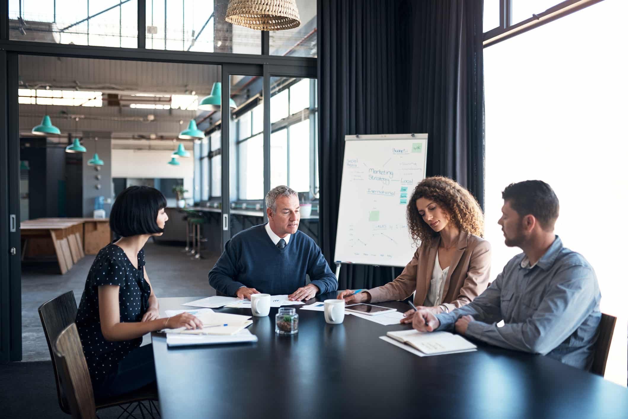 Four people discuss compensation strategy consulting at a conference table with papers and coffee.