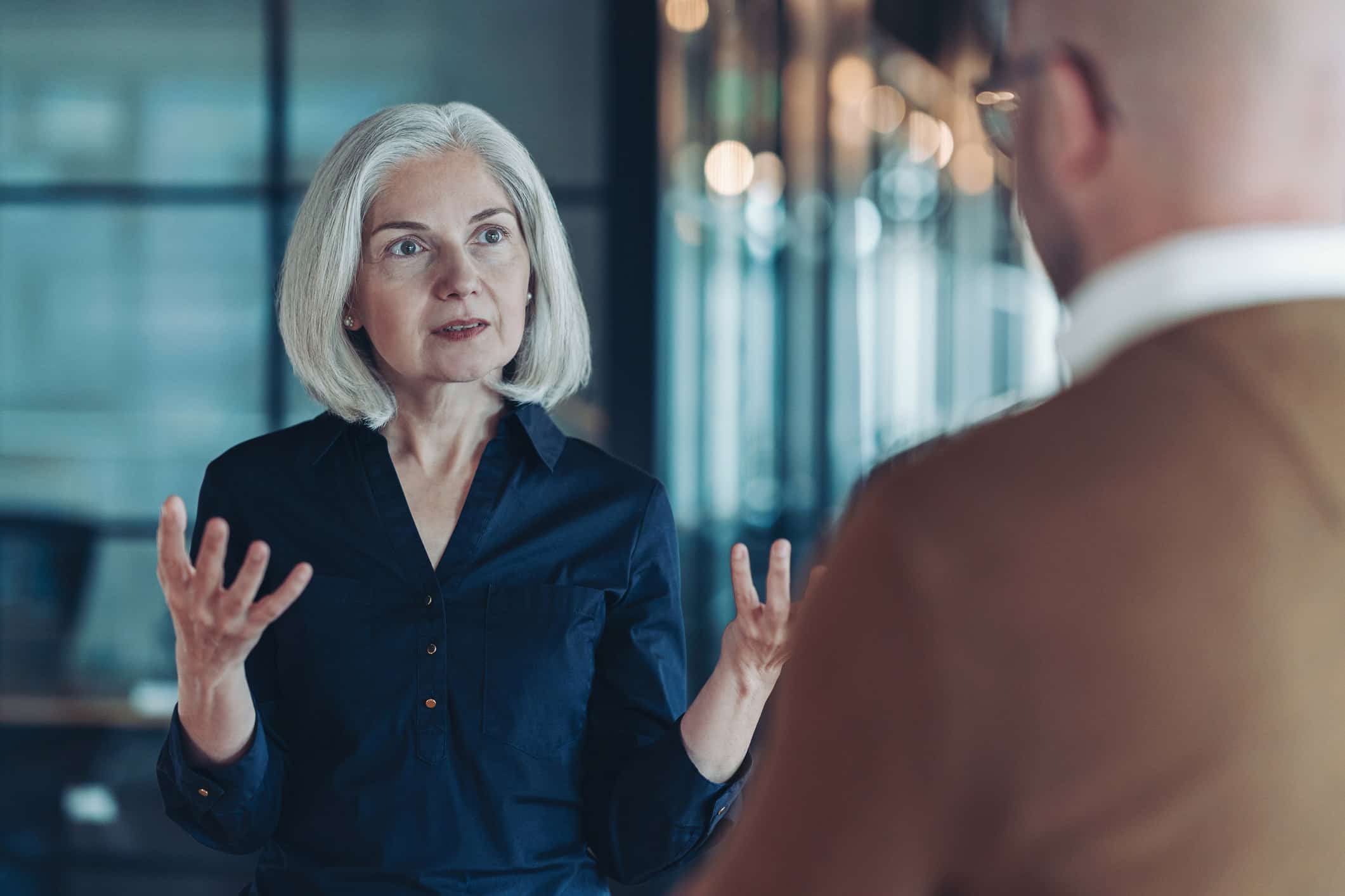 Older woman with gray hair discusses with a man in an office about law firm pricing strategy.