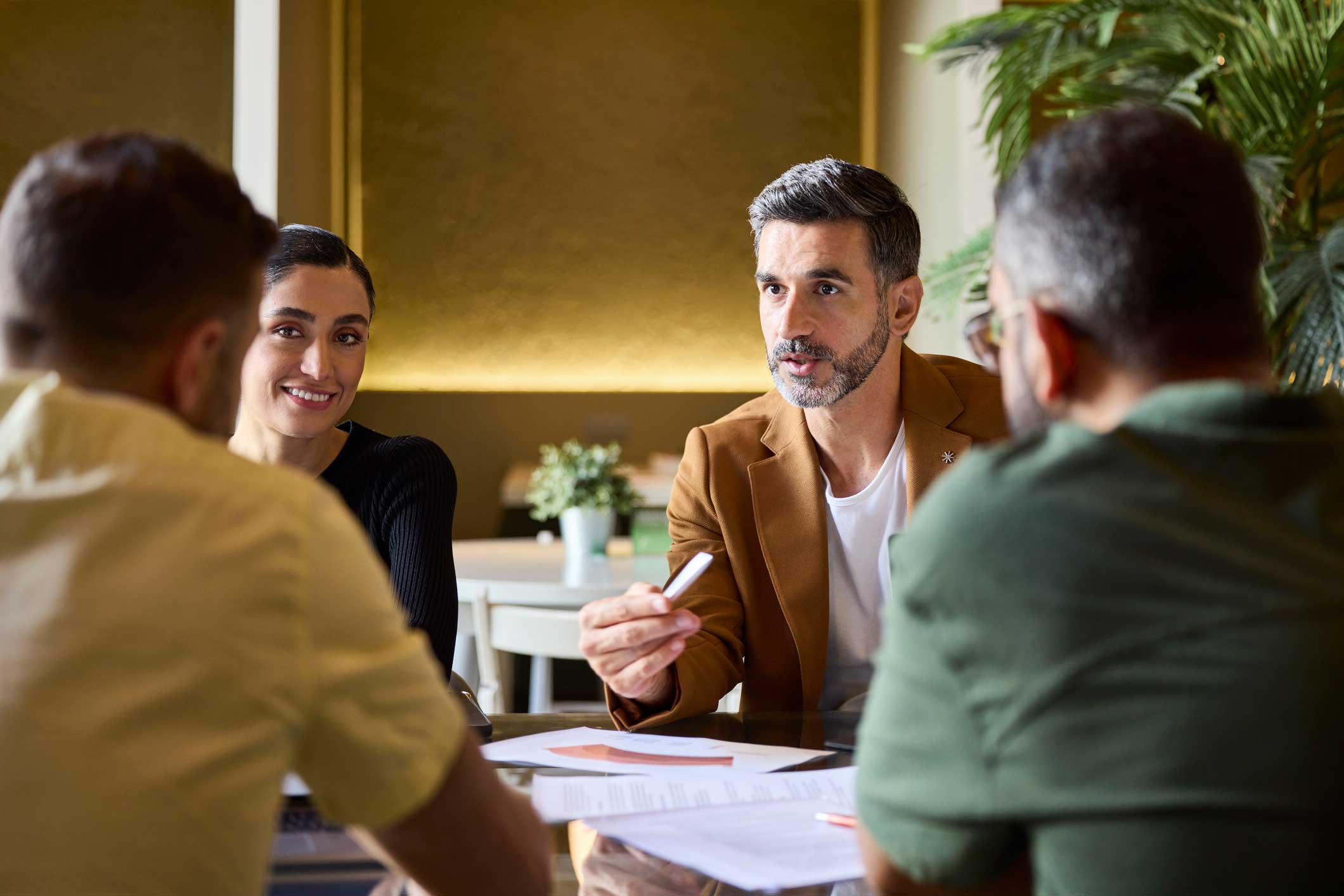 Four people discuss Mobility Strategy Consulting at a table with papers and plants behind them.