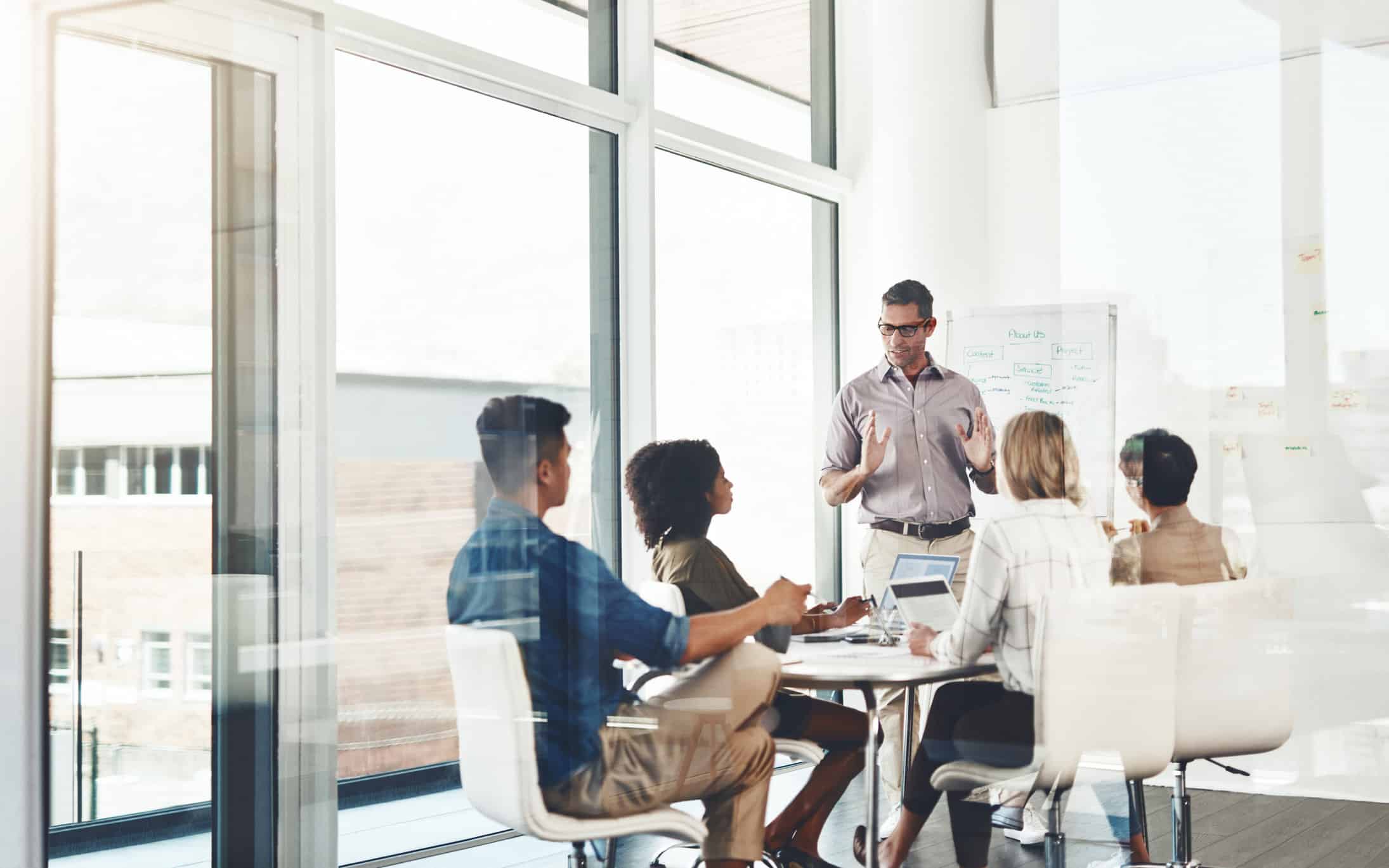 Five people have a witness preparation meeting in an office with large windows and a whiteboard.