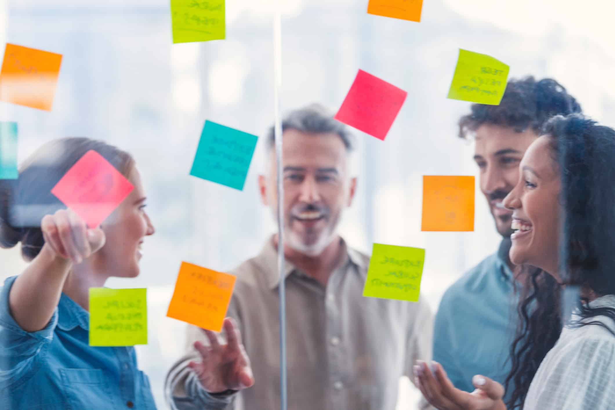 Four people discuss Operational Alignment with colorful sticky notes on a glass wall.