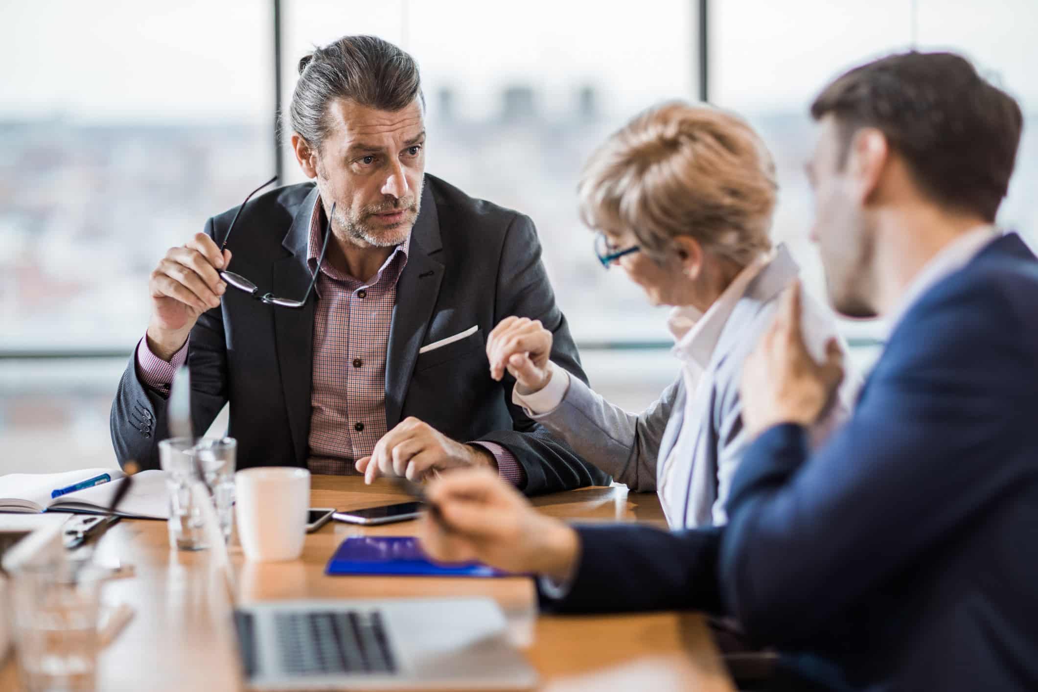 Three business people discuss Real-Time Analytics Consulting at a meeting table in an office.