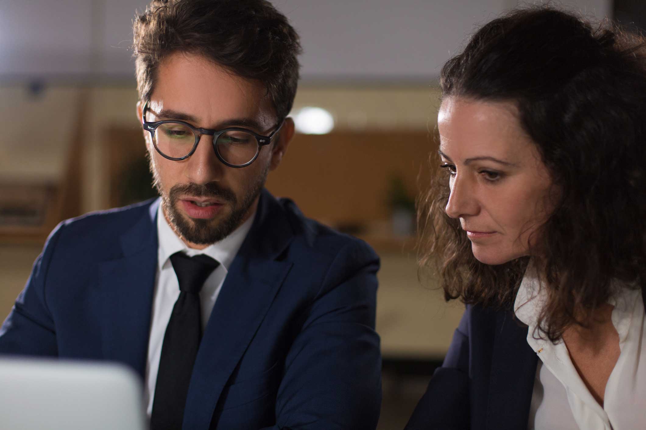 Two business professionals in suits discuss mobile device management advisory over a laptop.
