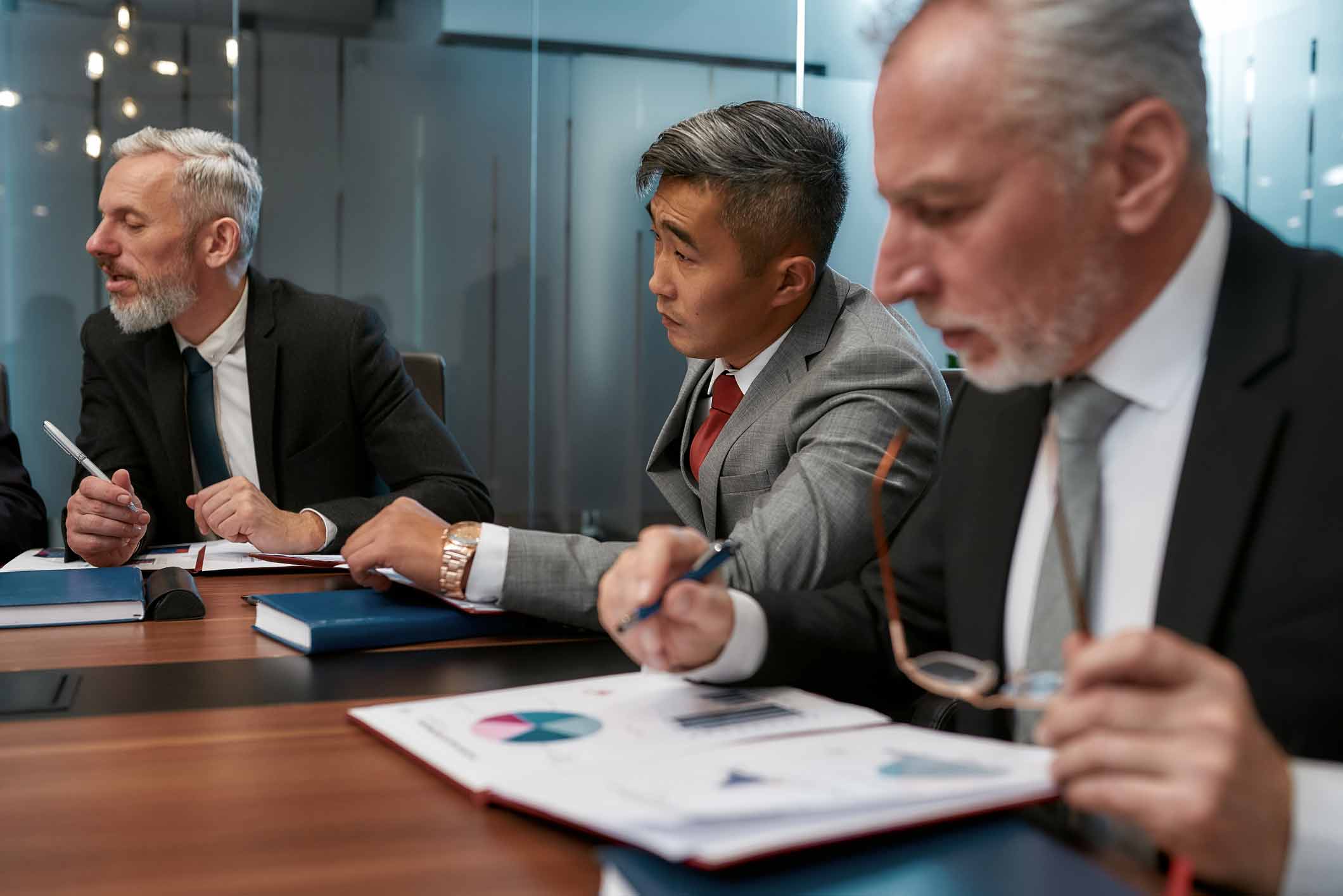 Three businessmen in suits discuss cyber incident response consulting services at conference table.