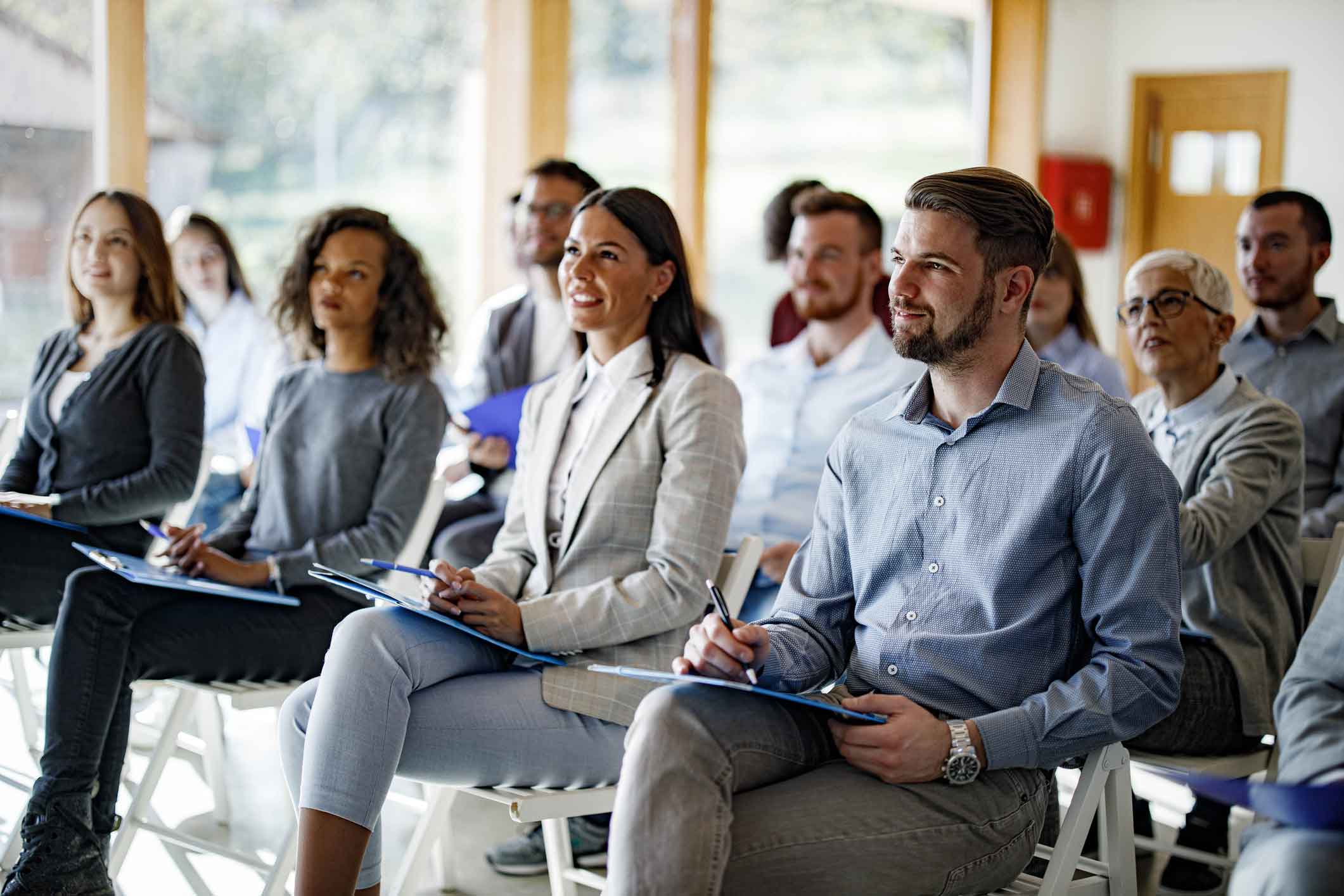 People sitting on chairs, smiling and taking notes during a cybersecurity compliance seminar.