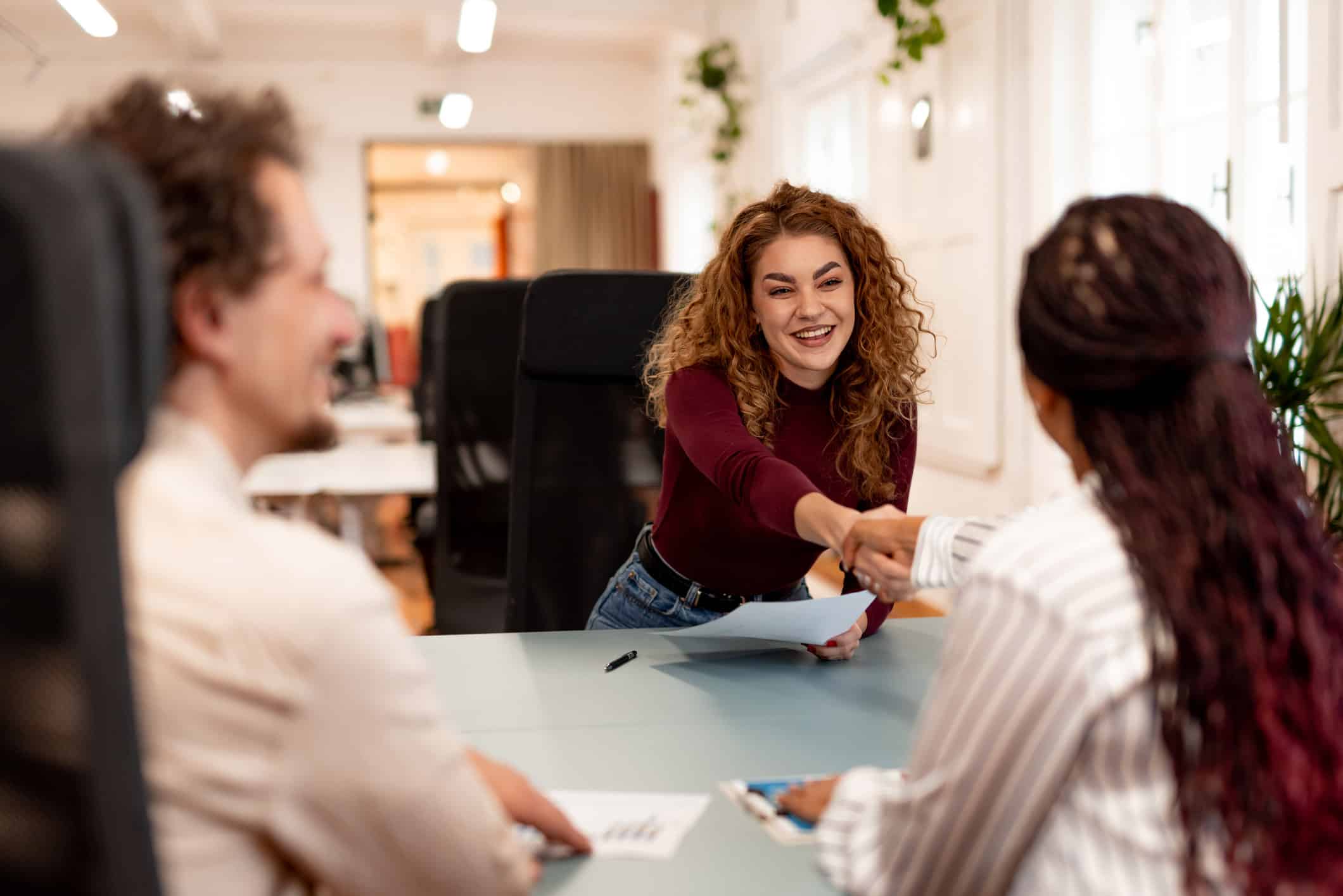 Woman smiling and shaking hands during an office meeting about an expense reduction strategy.