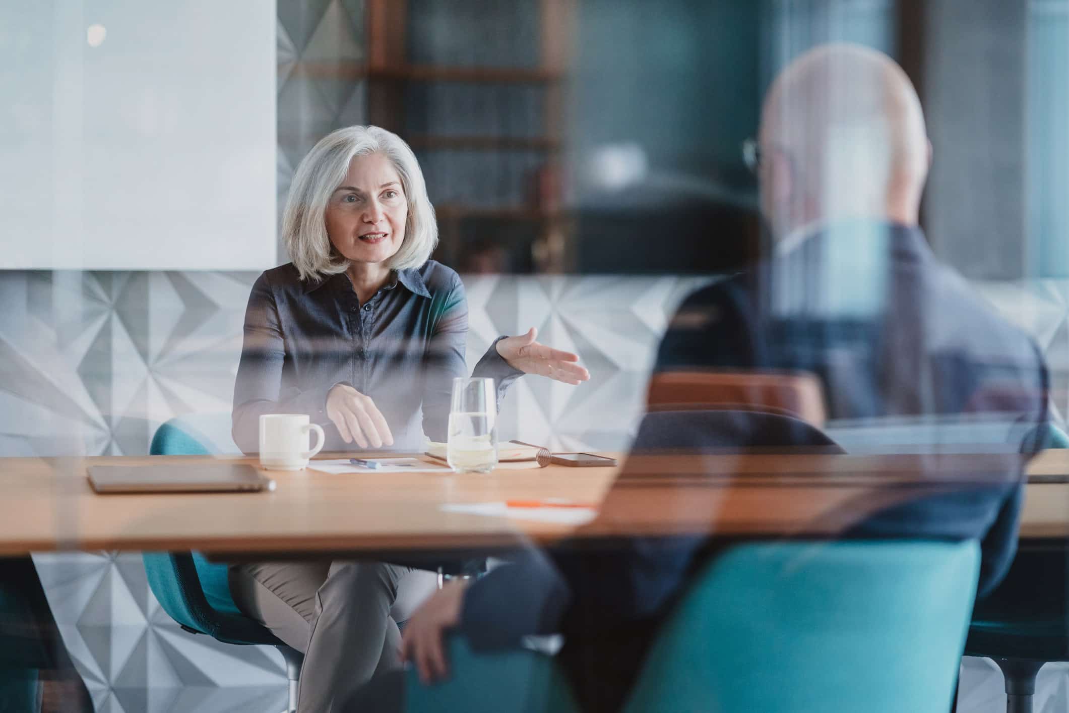 Older woman discusses Practice Mix Optimization Consulting across a modern conference table.