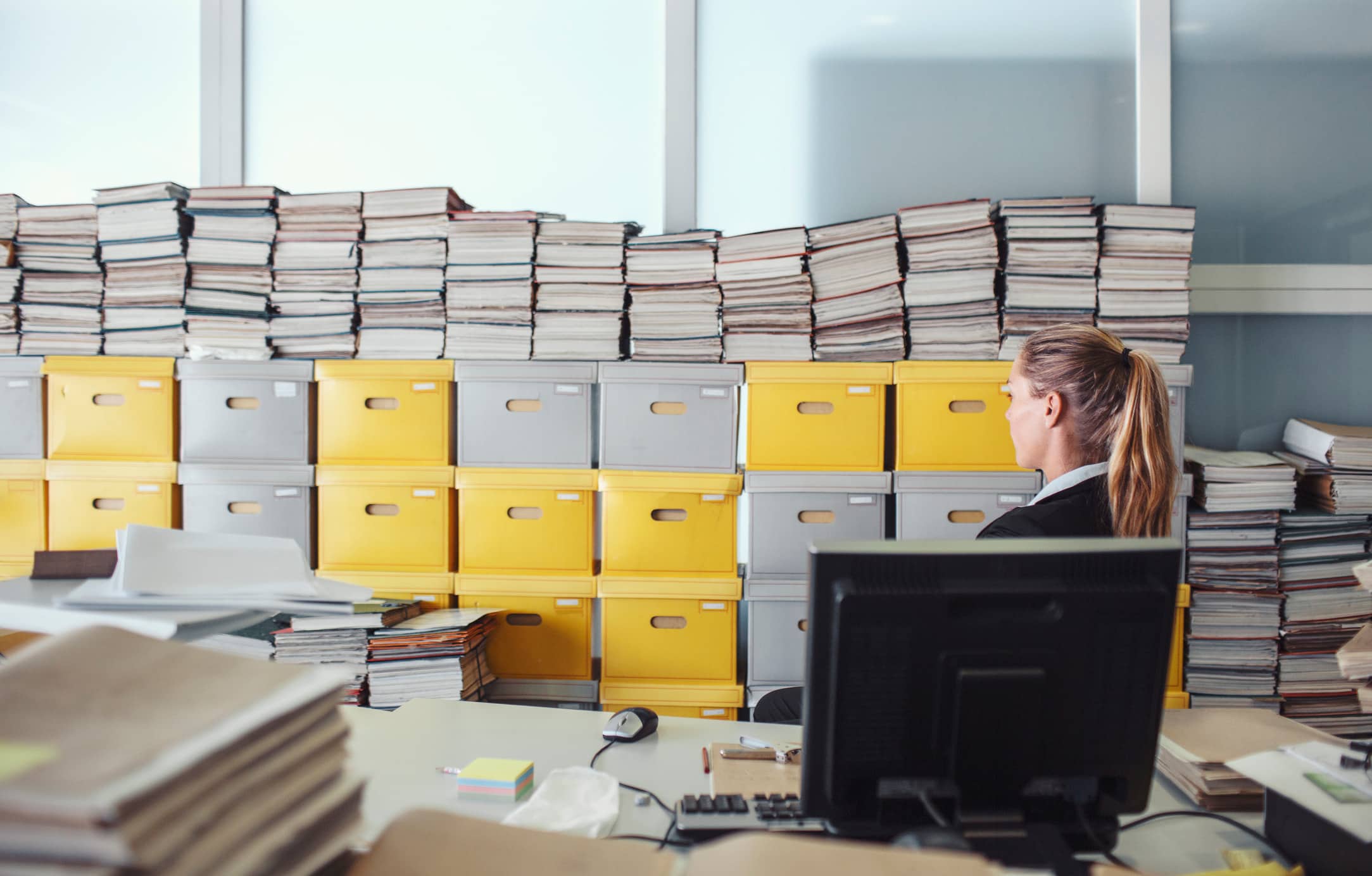 Woman at desk with computer, files, and yellow boxes, focused on eDiscovery data analysis.