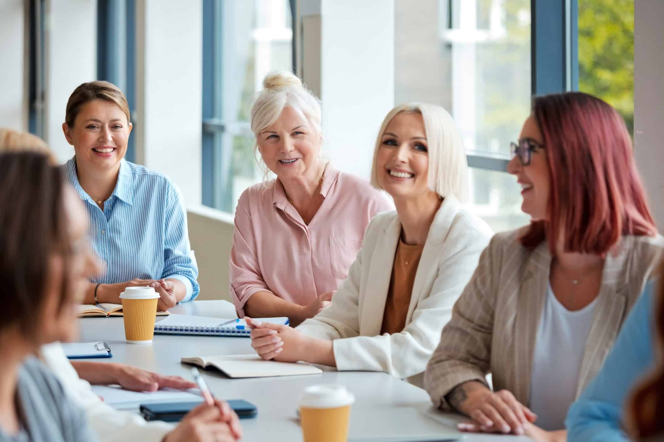 Five women discuss Partner Compensation & Succession Planning over coffee at a meeting table.