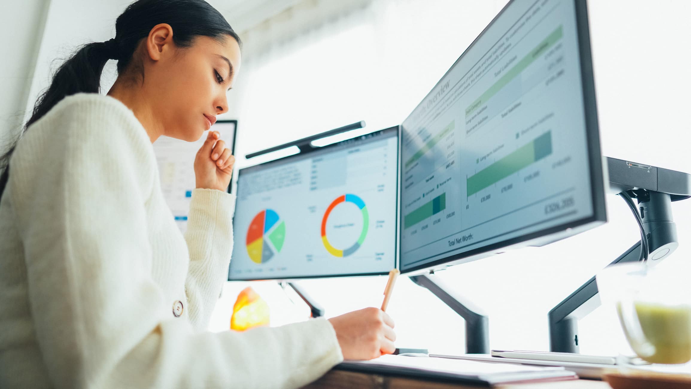 Woman analyzing charts on dual monitors, focused on TAR Model Optimization at her desk.