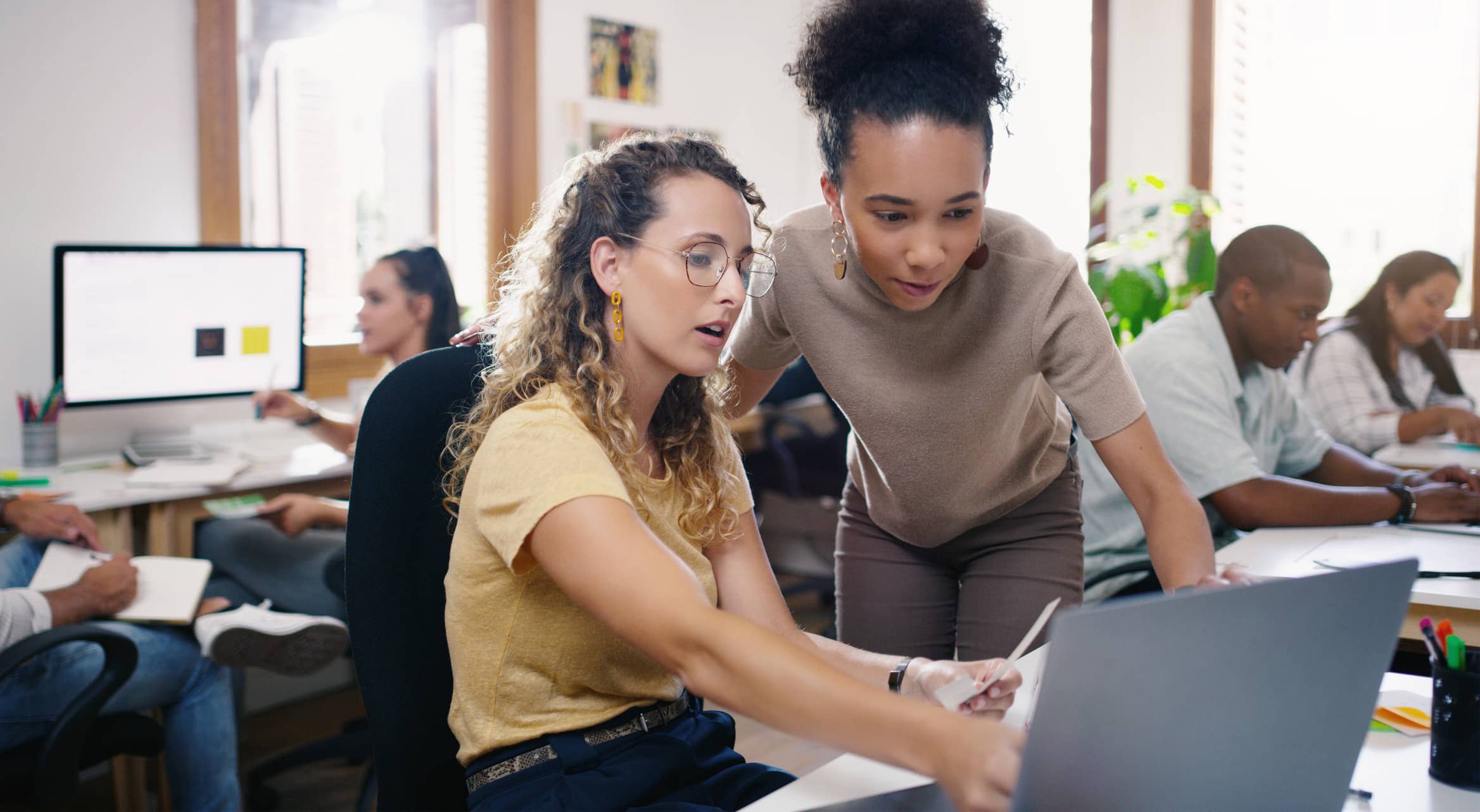 Two women collaborating on TAR Platform Integration at a desk in a busy office environment.