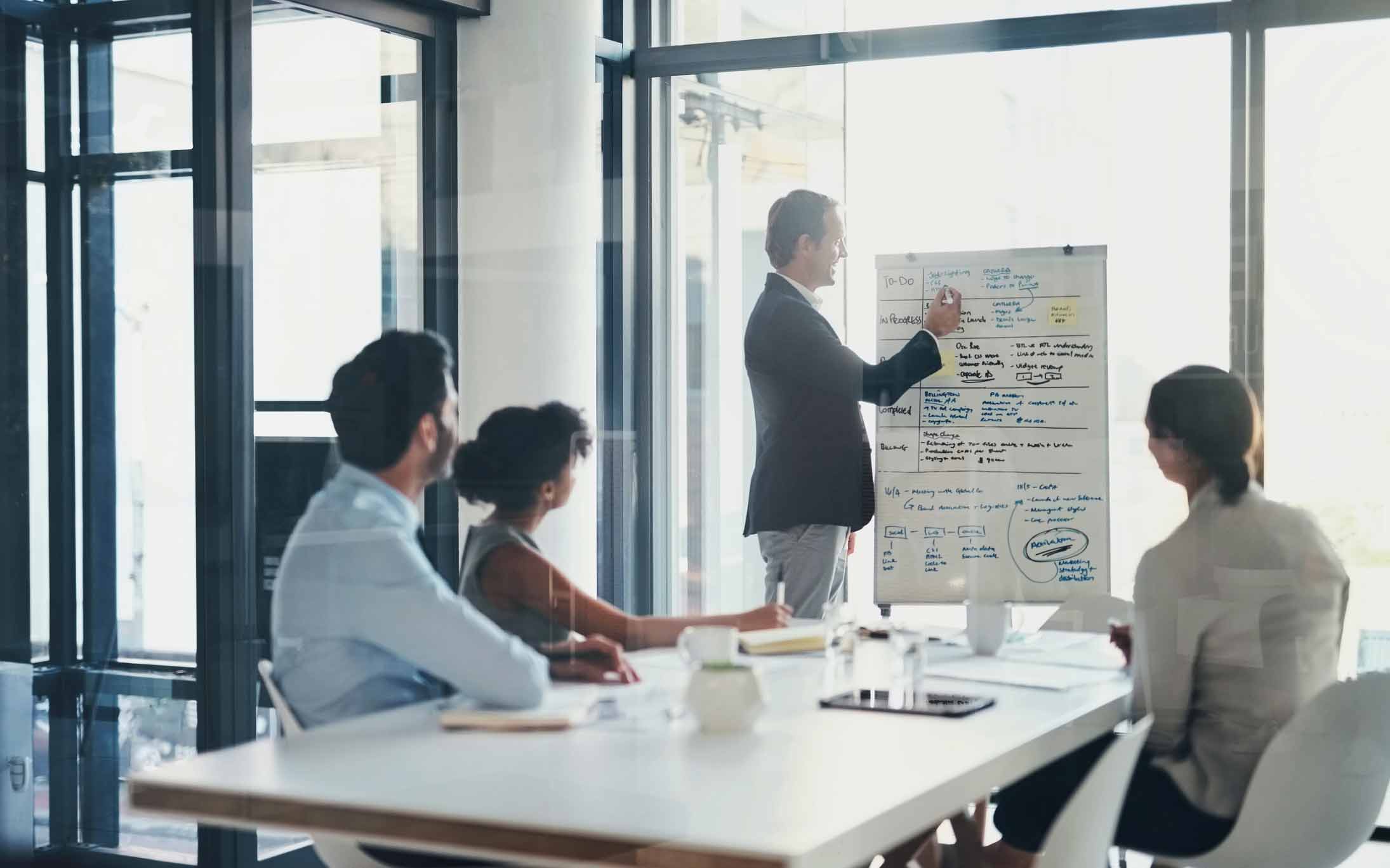 Man presenting notes on a flip chart about document management to three colleagues in a modern office.