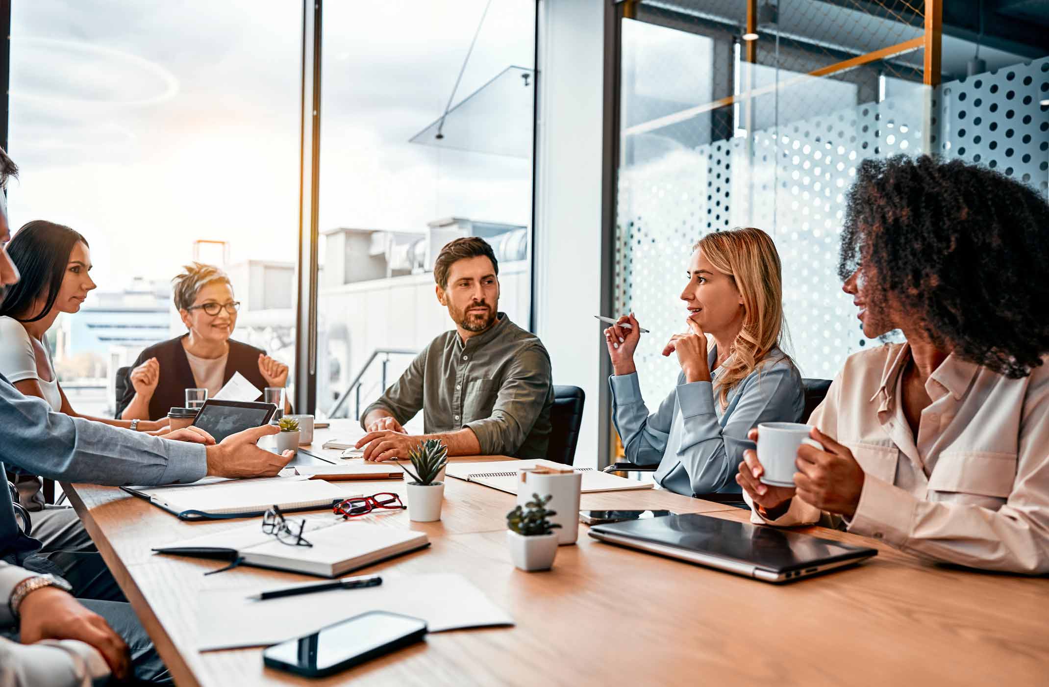 Six people discuss Policy Design at a meeting table, working with laptops, papers, and coffee.