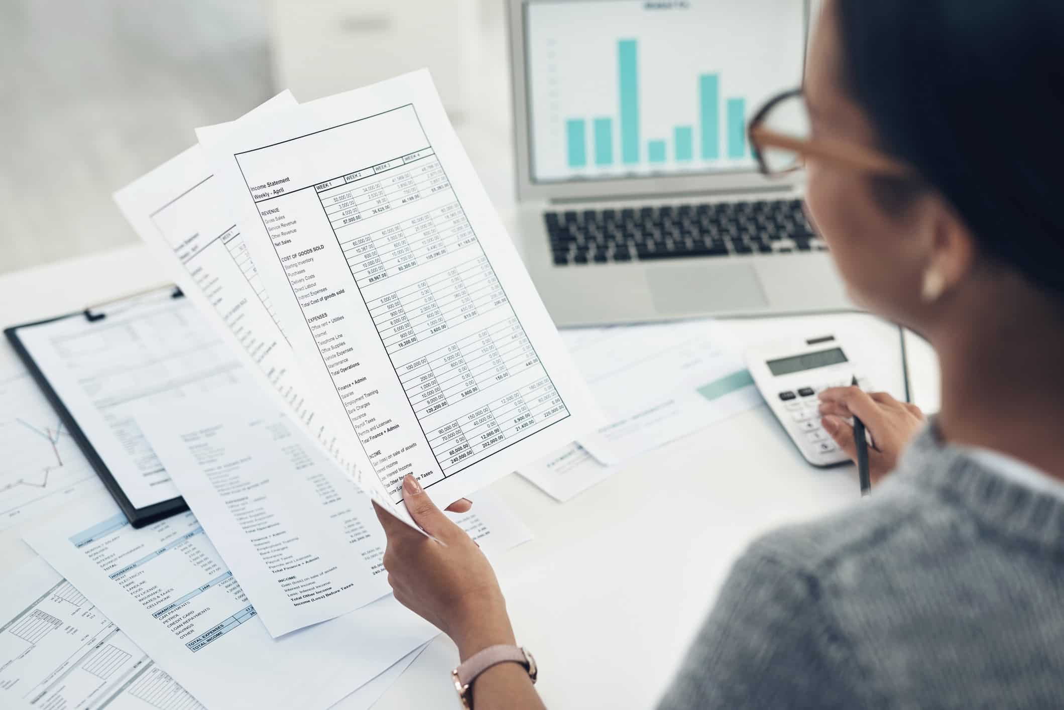 Person reviewing financial documents for Corporate Tax Consulting Services at a desk with a laptop.