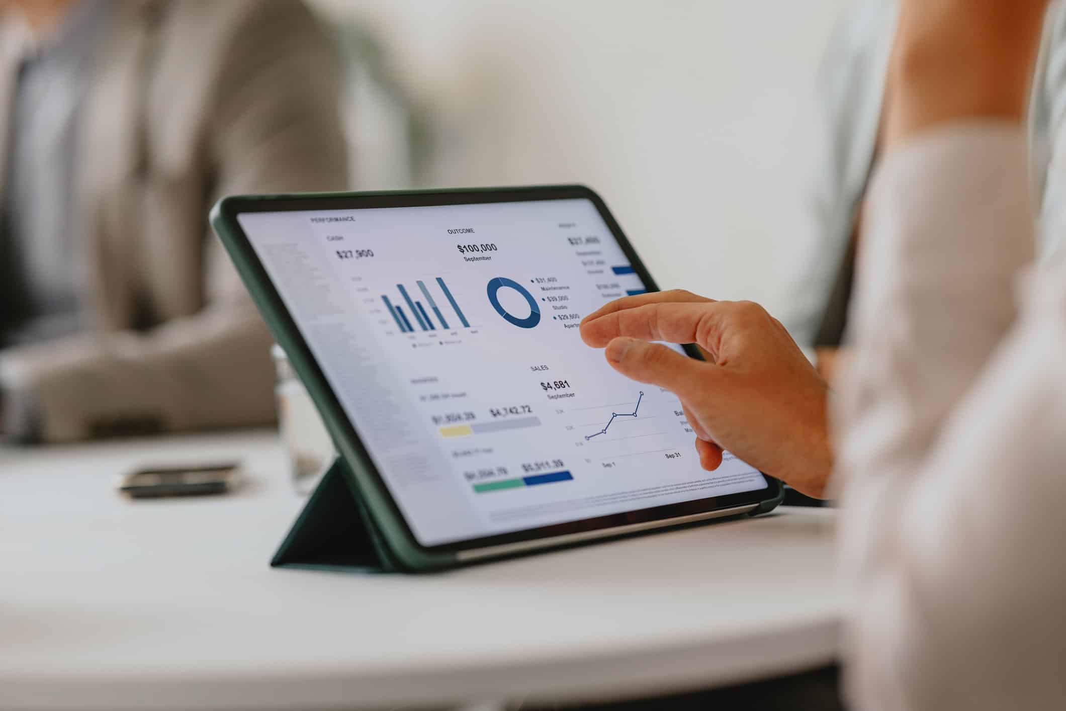 Person using a tablet displaying Law Firm Portfolio Analysis graphs and financial data at a table.