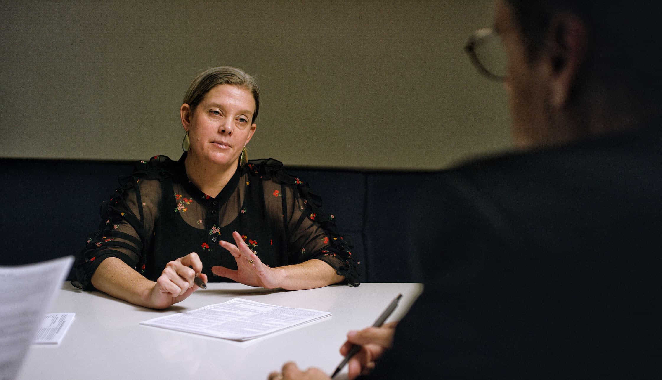 Woman in black blouse discusses Economic Damages Advisory across table with documents and pens.