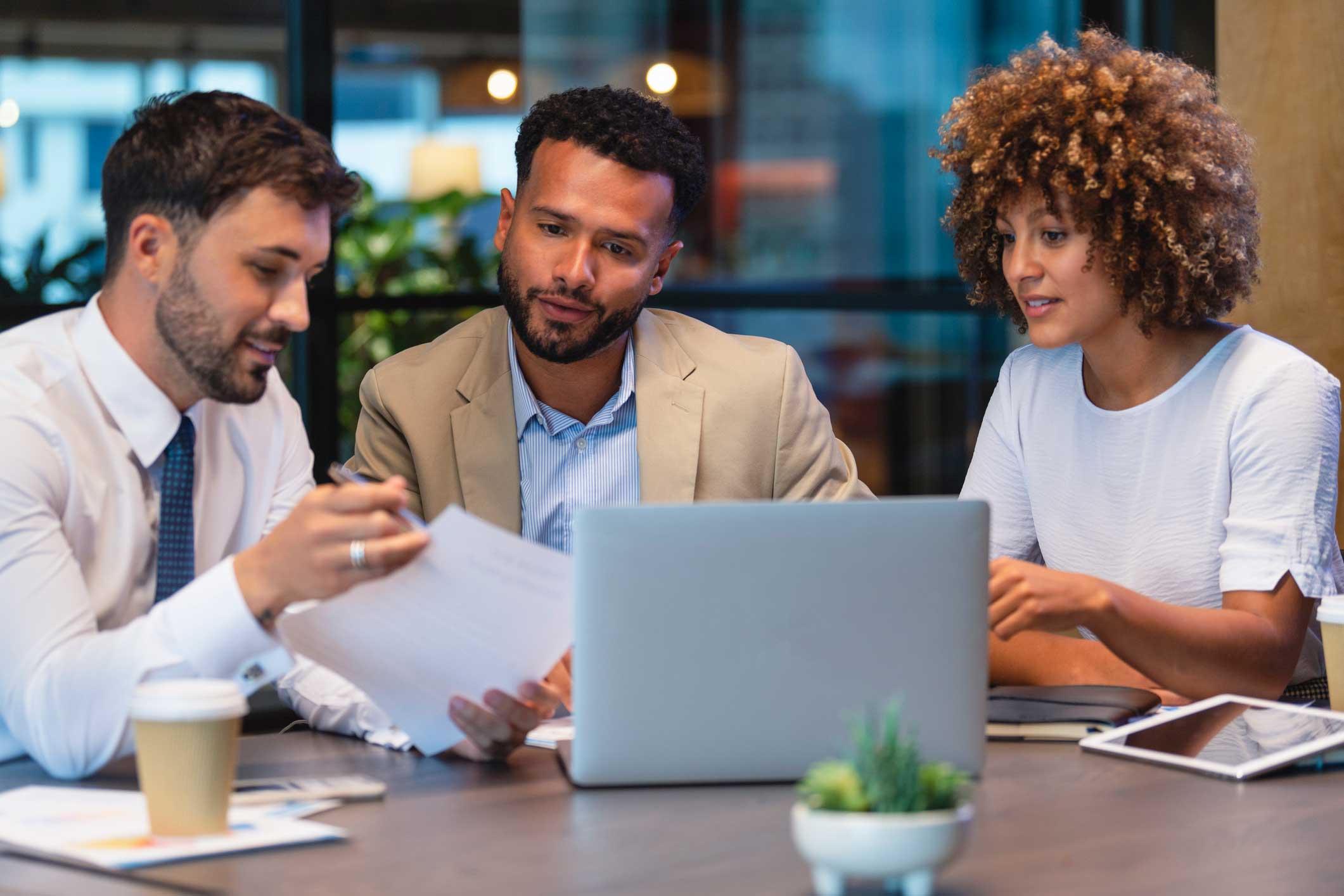 Three people discuss IT disaster recovery documents in a modern office, emphasizing governance.