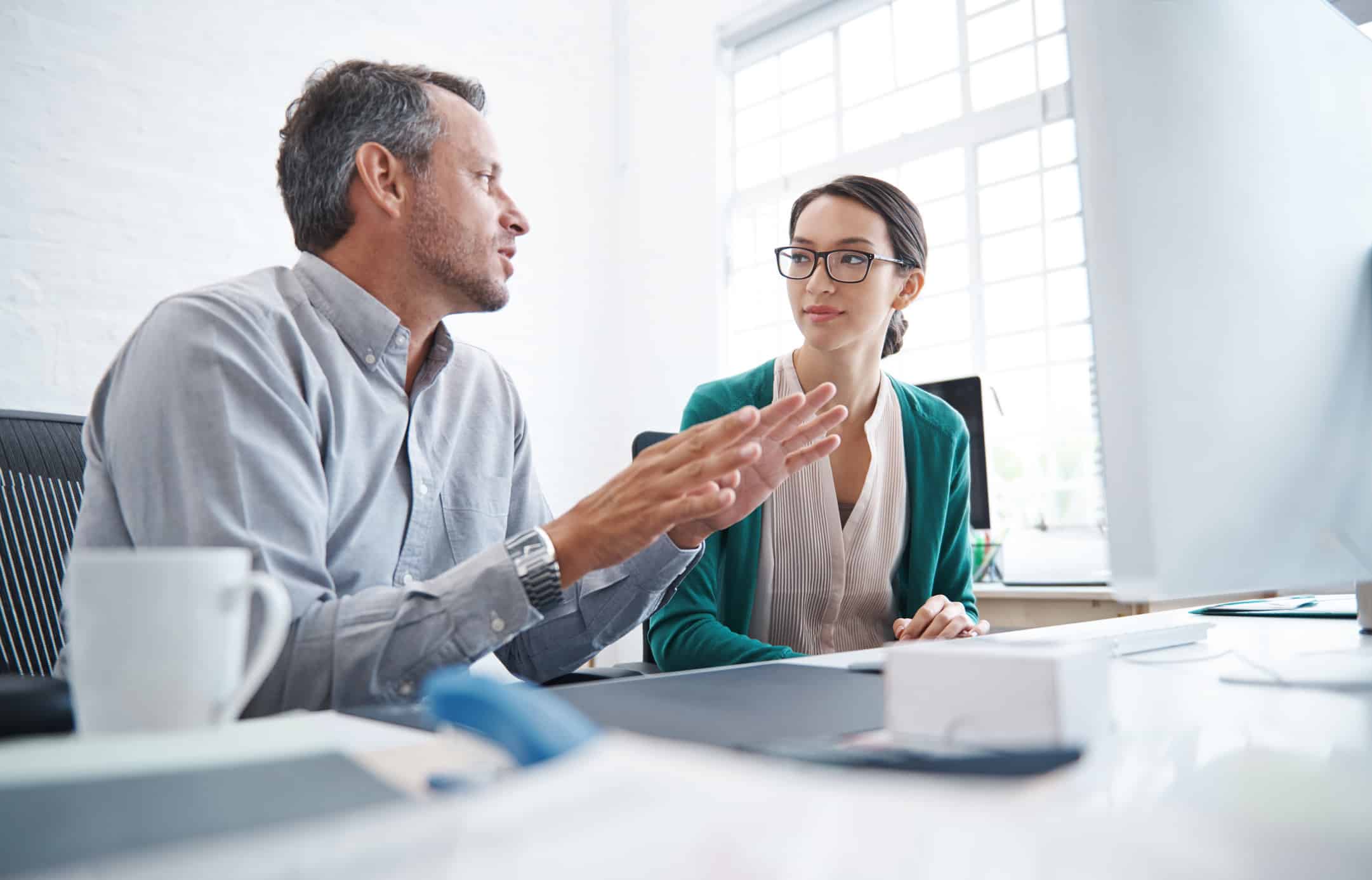 Two colleagues discussing quality control and audit readiness at a desk in a bright office.