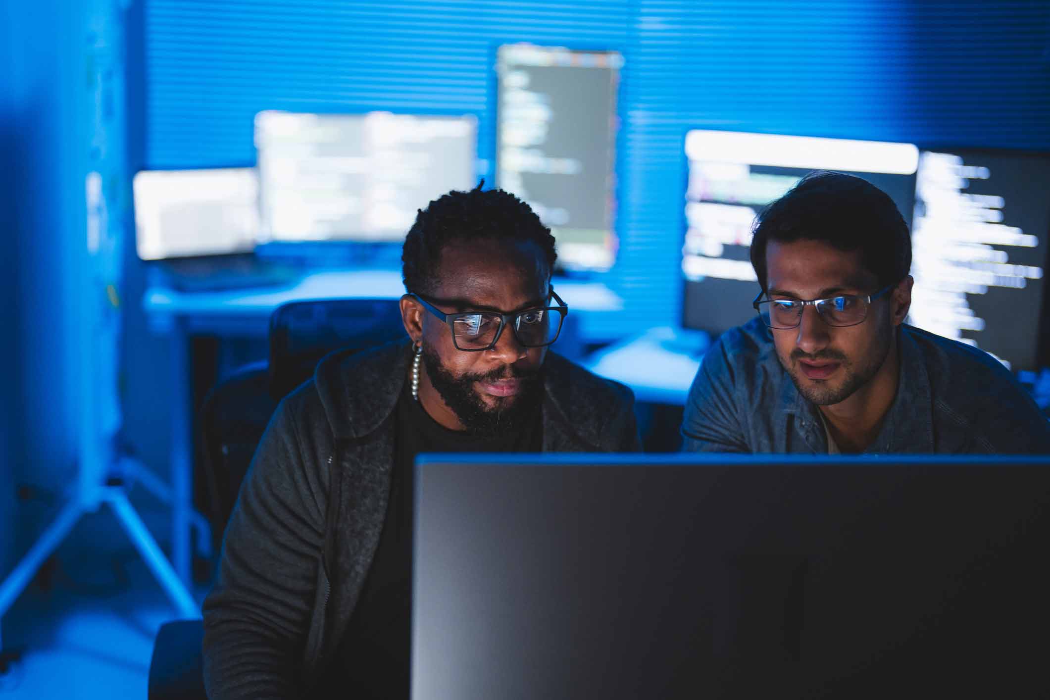 Two men coding together at a computer, consulting on data breach advisory in a dimly lit room.