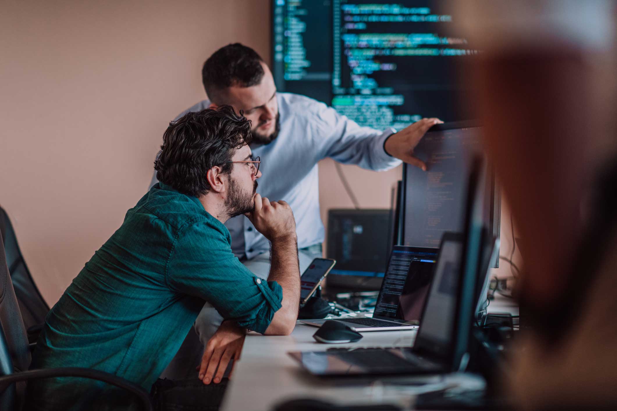 Two men collaborating on cyber incident response triage at computers in an office setting.