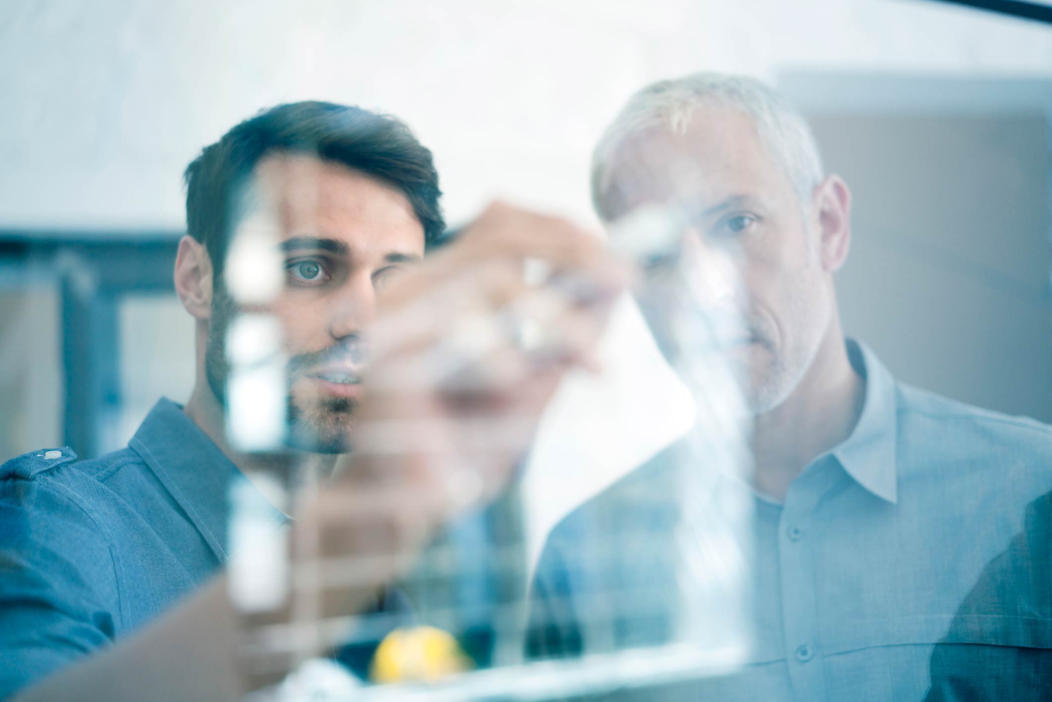 Two men developing workflow automation on a transparent board, focused on their work.