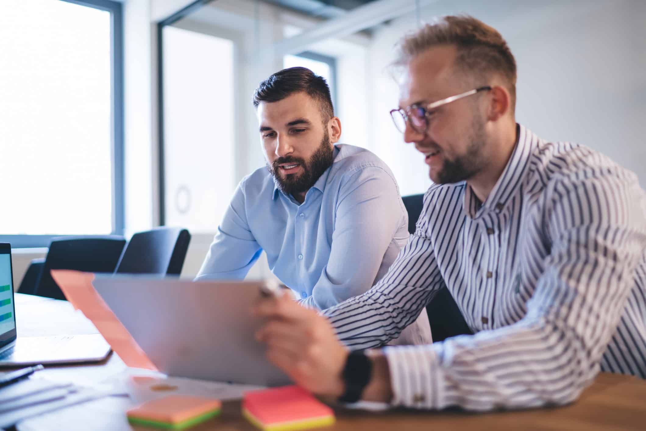 Two men collaborating on healthcare litigation support at a desk with a laptop and sticky notes.
