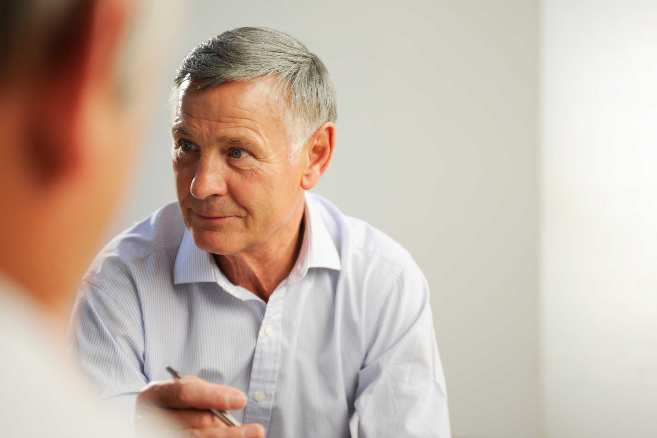 Older man in a light shirt listens attentively to an email security advisory in a bright room.