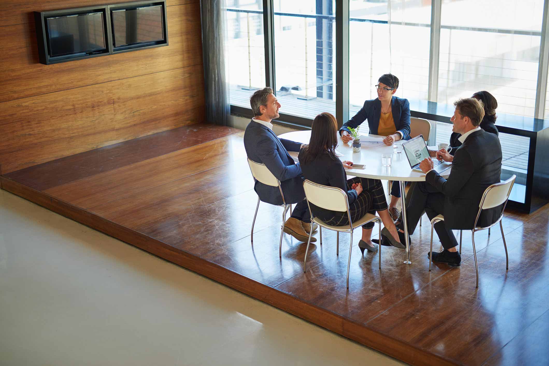 Five people in business attire meet at a Document Management Consulting Firm’s modern office table.
