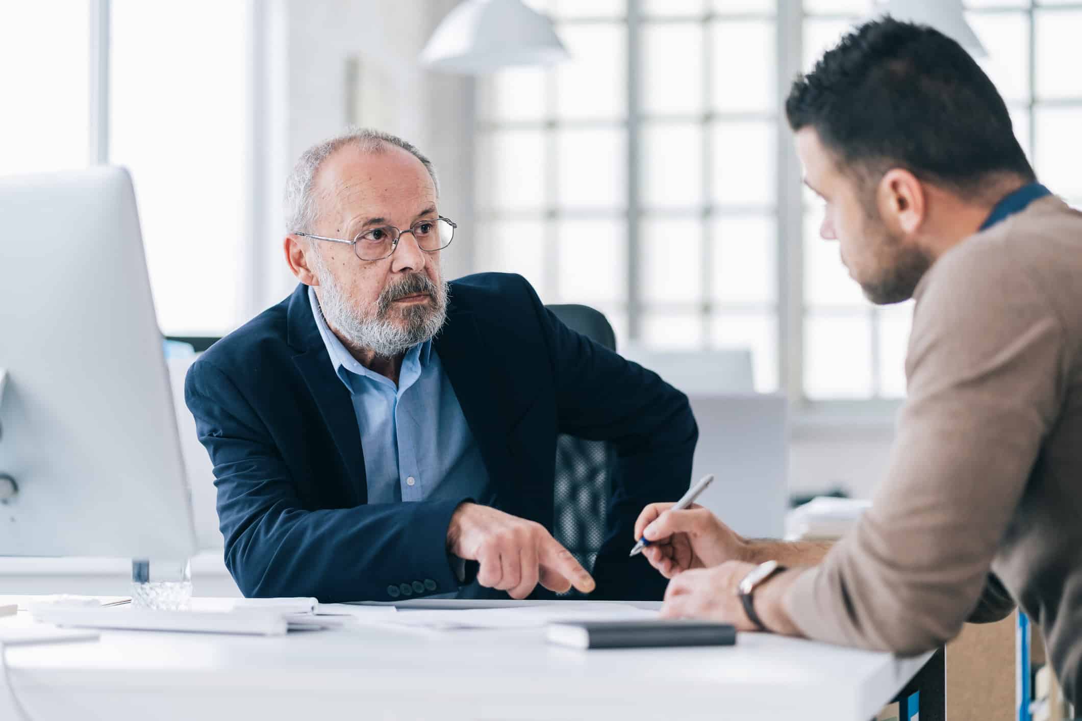 Older man in a suit discusses Data Governance Consulting Services with a younger man taking notes.