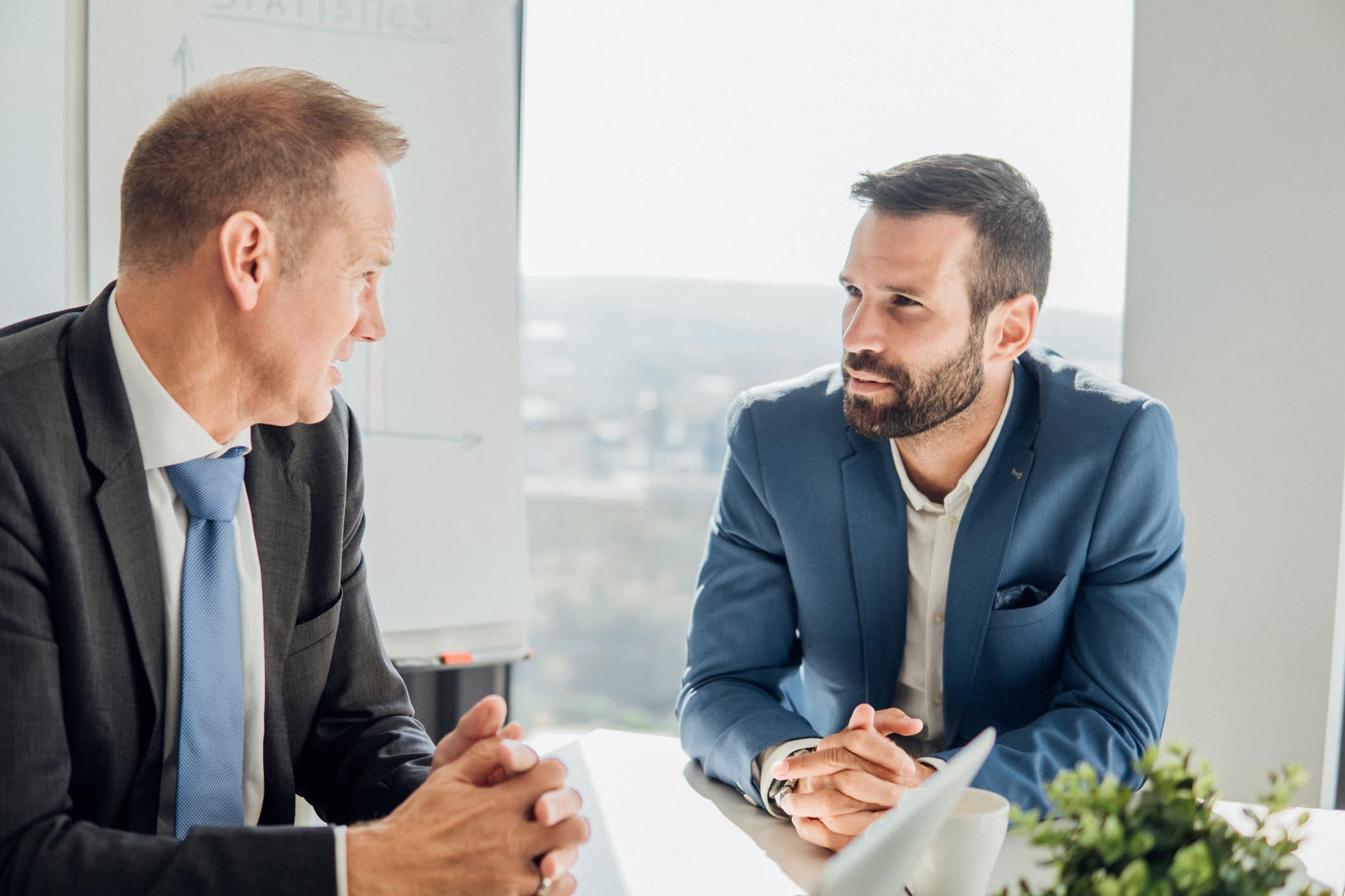Two men in suits discuss business at a Mergers & Acquisitions Consulting Firm office.
