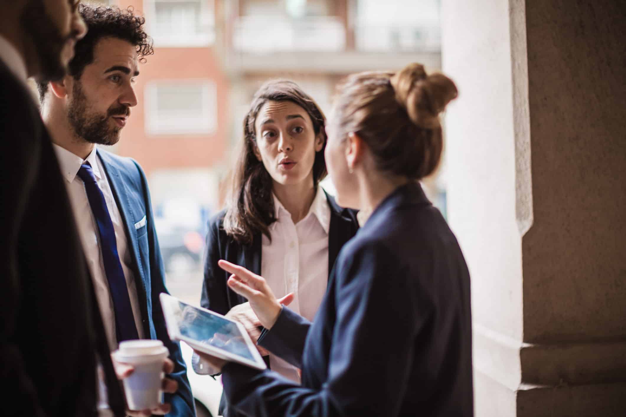 Three professionals discussing M&A Strategy Advisory, one with a tablet and another with coffee.